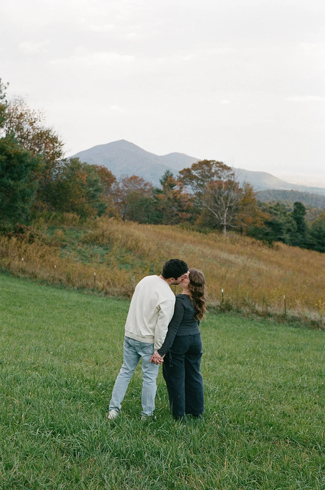 woman and man kissing in a meadow with a mountain behind them