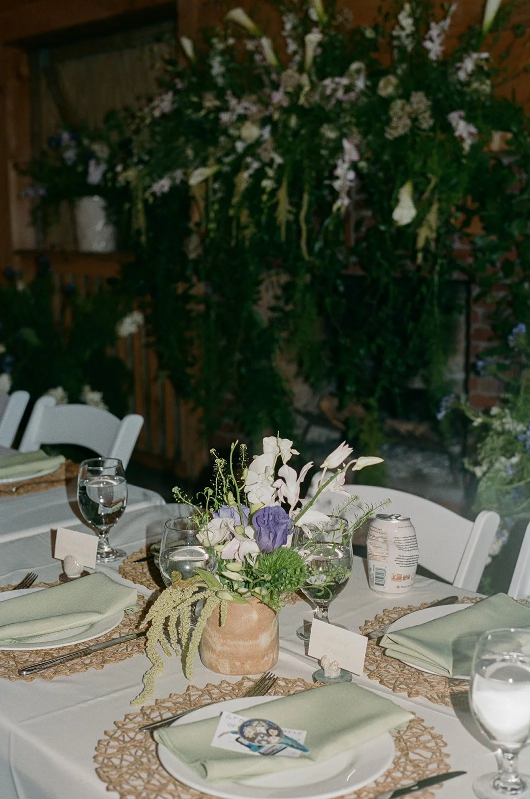 A table set for a meal with a floral centerpiece, photos, glasses of water, and place settings in a decorated room with wall-mounted plants. ocracoke outerbanks wedding film photographer
