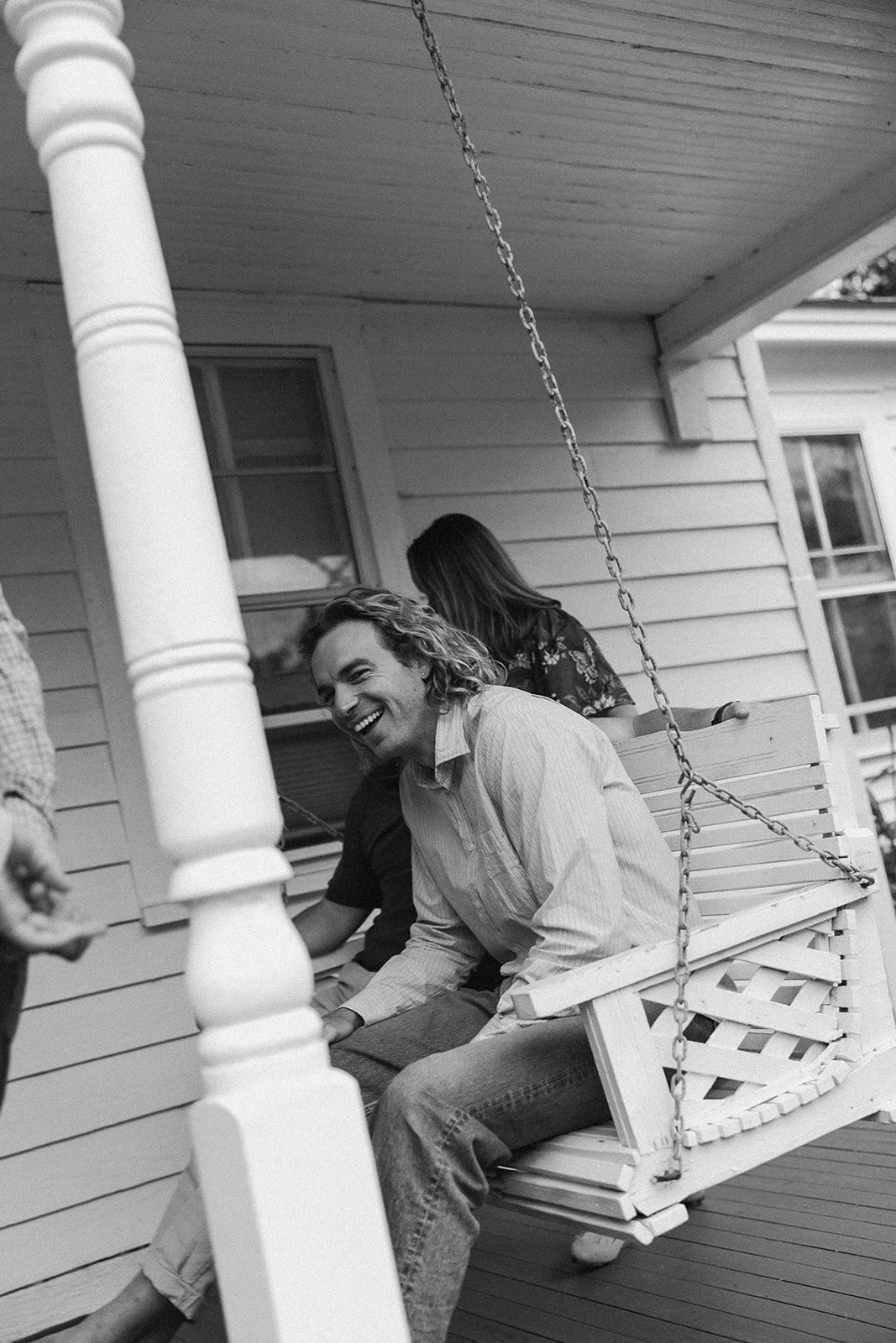 People sitting on a porch swing in front of a house, laughing and socializing. ocracoke outerbanks wedding film photographer