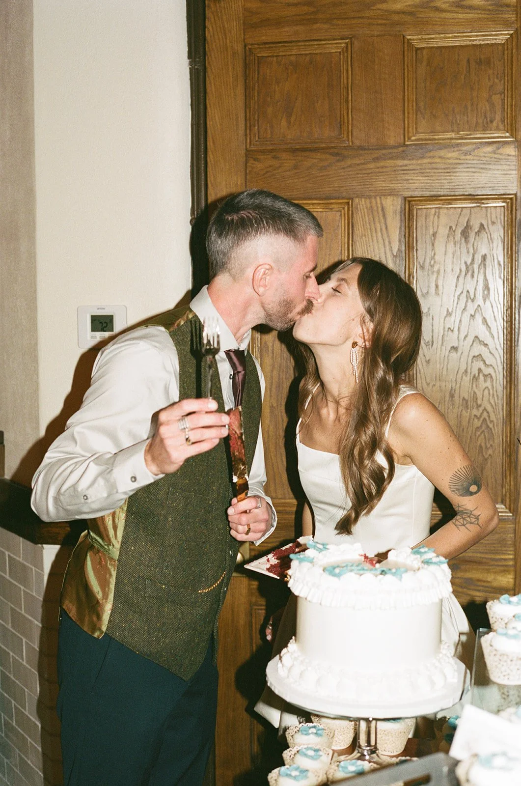 A couple kissing at a wedding reception, with a wedding cake and desserts in the foreground. roanoke wedding film photographer virginia