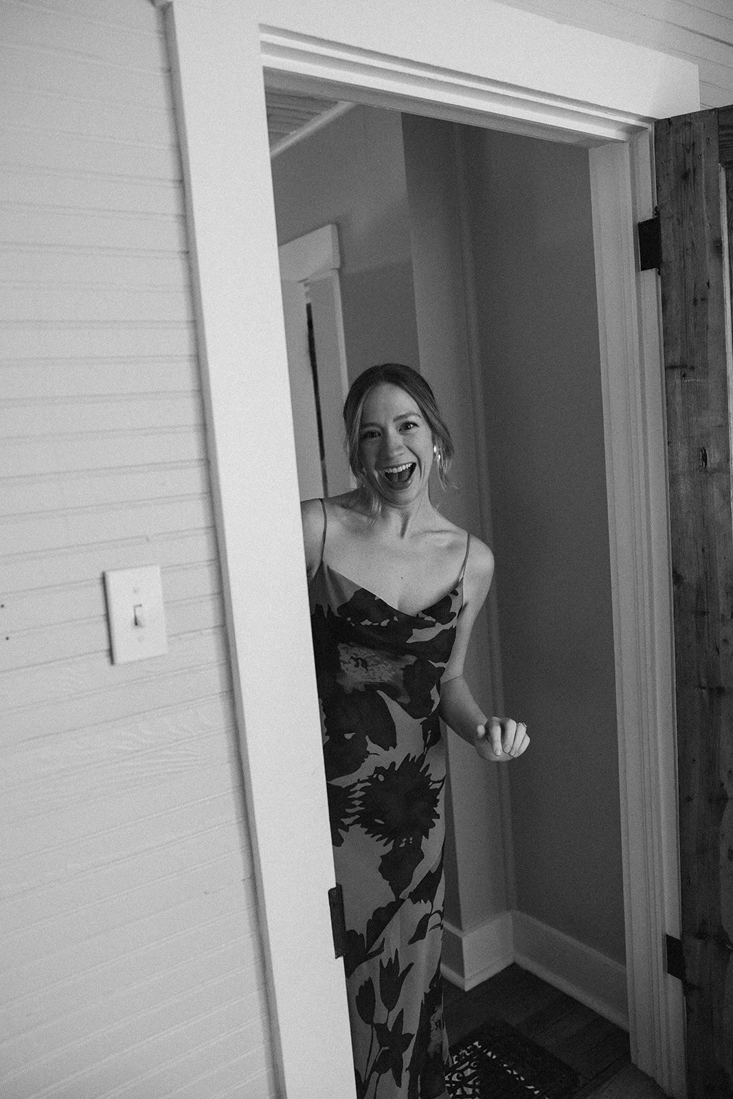 A woman in a floral dress is smiling and peeking out from behind a door. charlottesville virginia Wedding Film Photographer