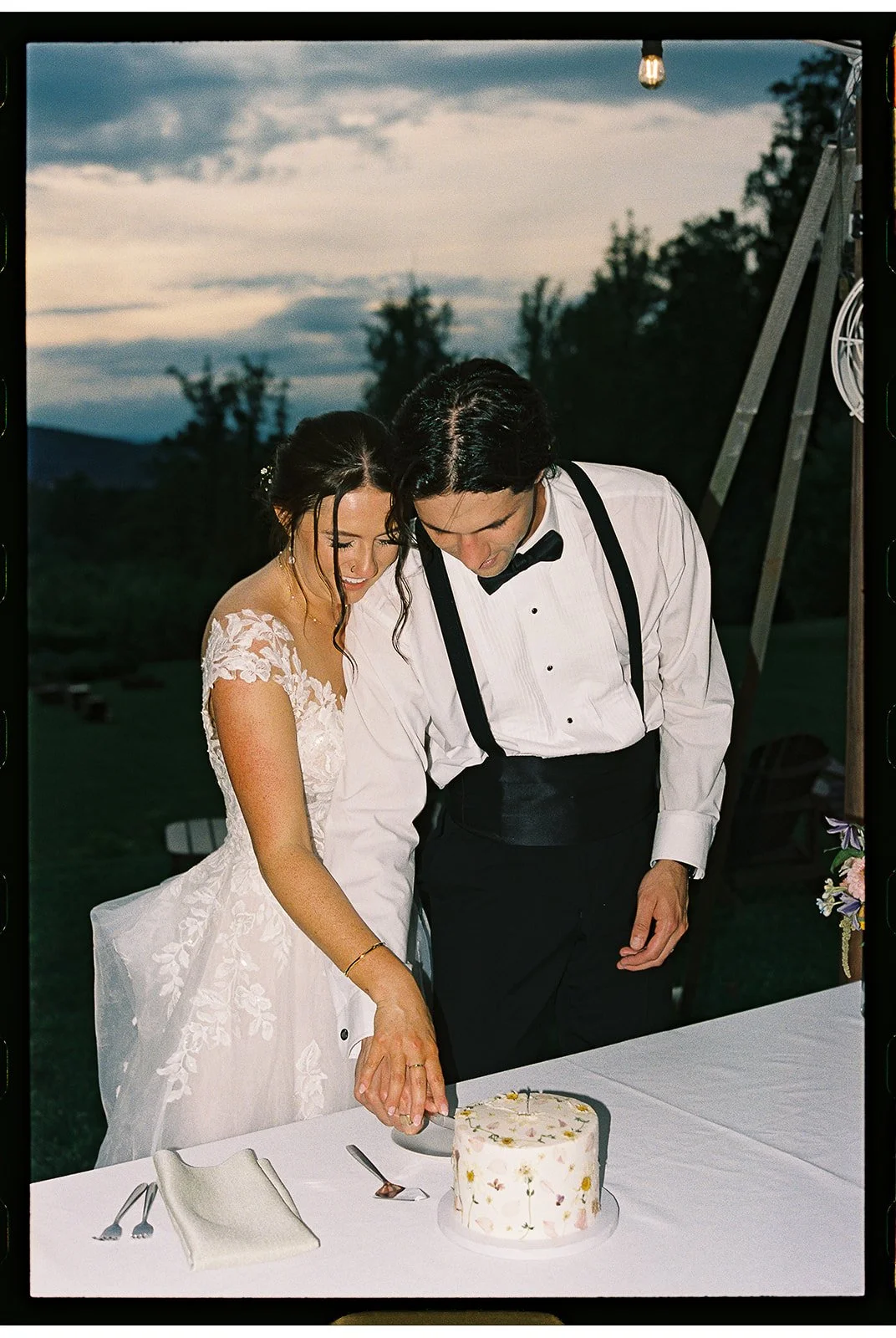 Bride and groom cutting a wedding cake outdoors at sunset, dressed in wedding attire with romantic lighting and countryside background. charlottesville virginia wedding photographer eastwood winery