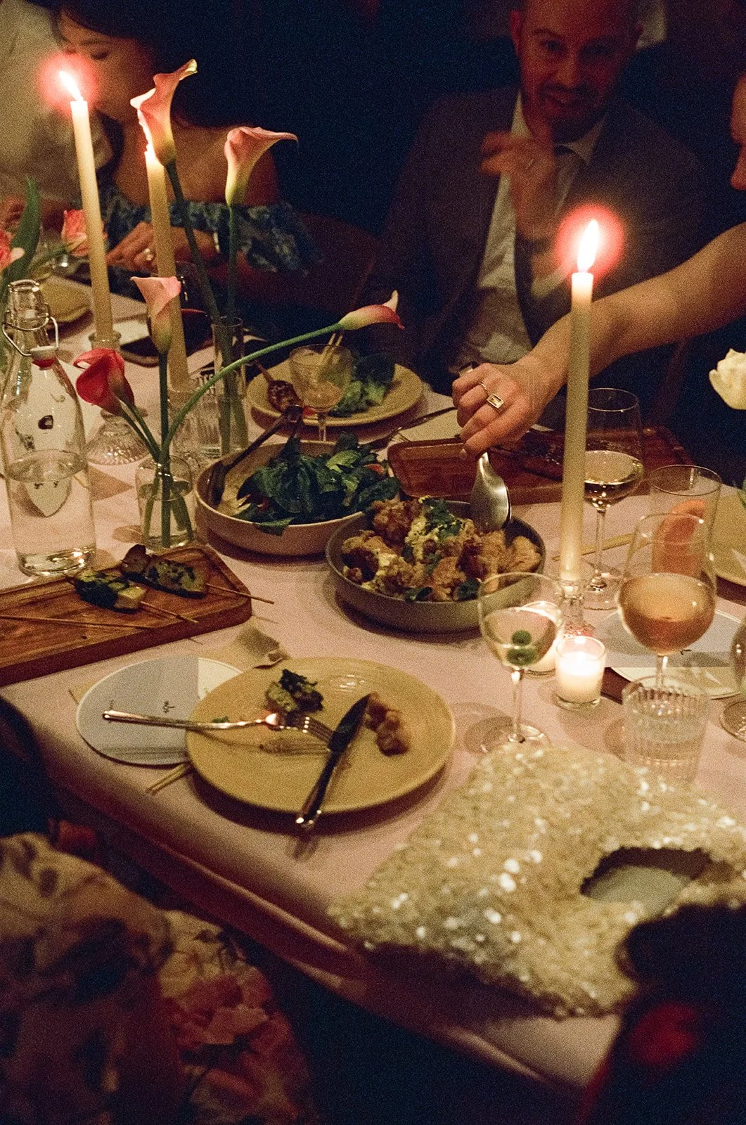 People celebrating at a dinner party with lit candles, flowers, and various plates of food on the table. rule of thirds brooklyn new york wedding film photographer