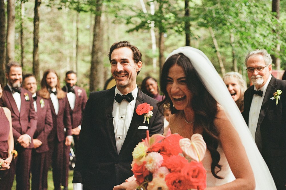 Bride and groom laughing at a wedding ceremony in a forest setting in Portland Maine, surrounded by the wedding party.