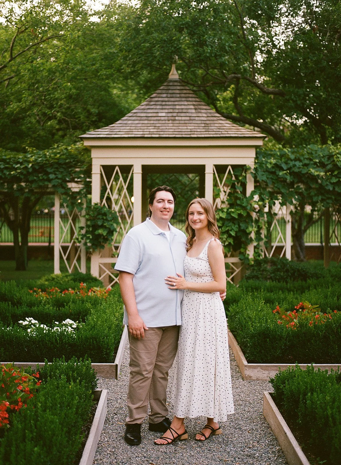 A couple posing in a garden with a gazebo surrounded by greenery and flowers. Old City Philadelphia engagement shoot