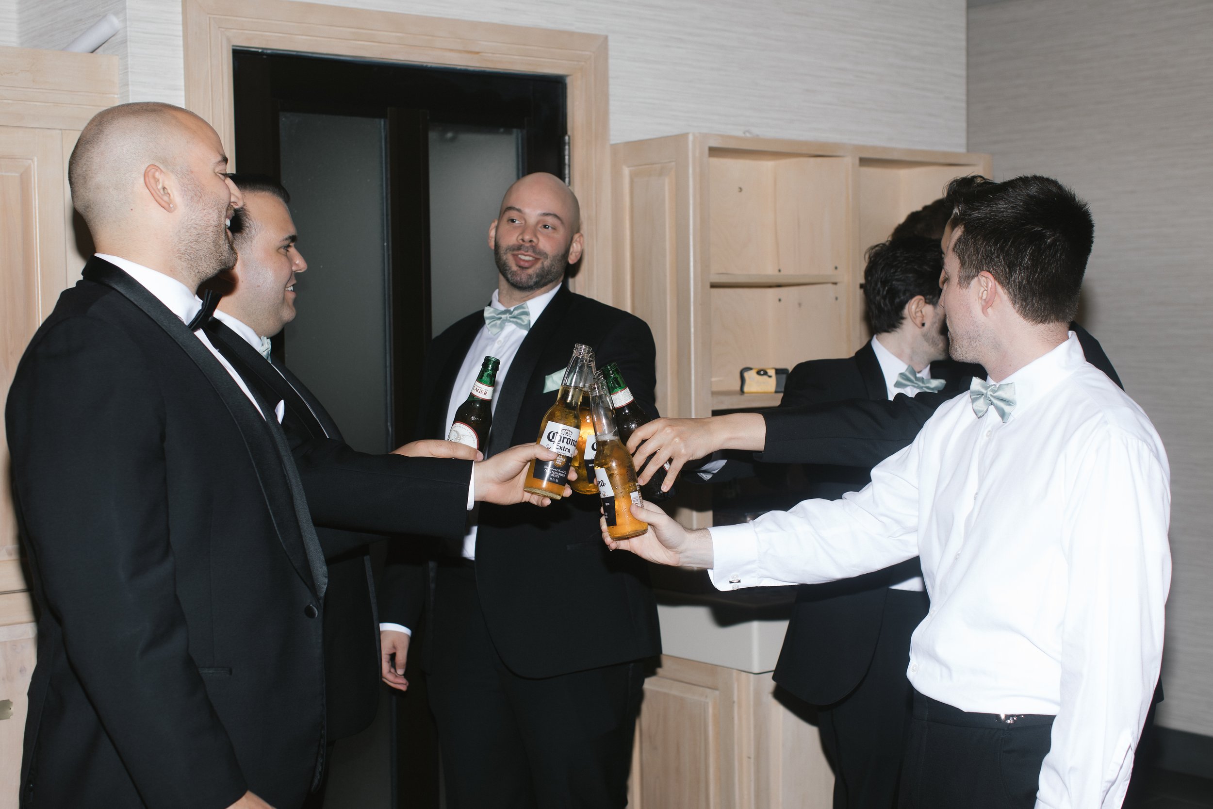 Group of men in formal attire toasting with beer bottles indoors. blue heron pines new jersey wedding