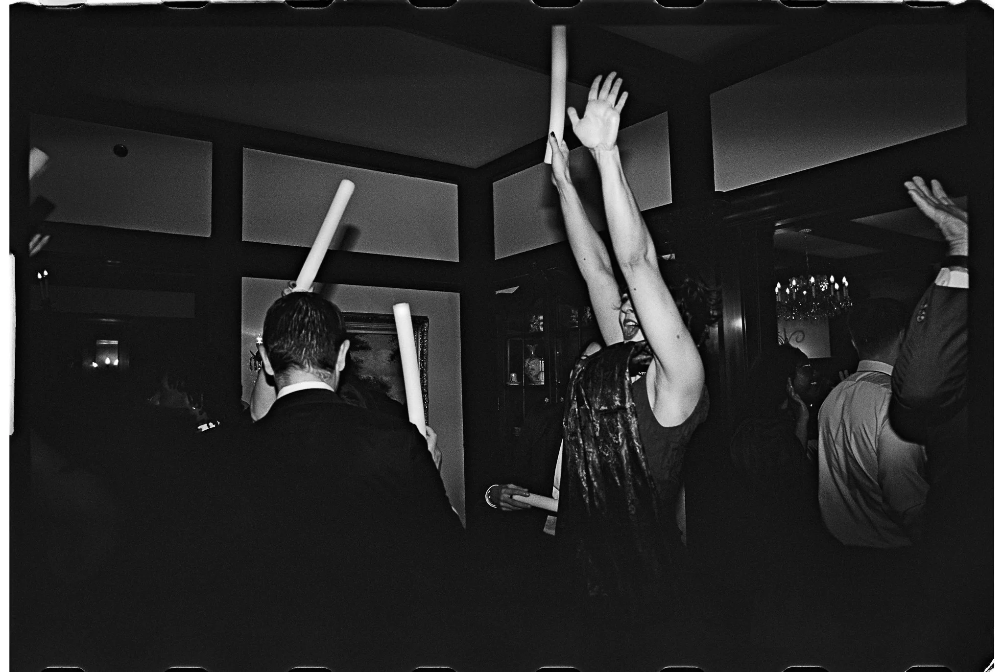 People dancing and raising hands with glow sticks at a party, black and white photo. gramercy mansion maryland wedding
