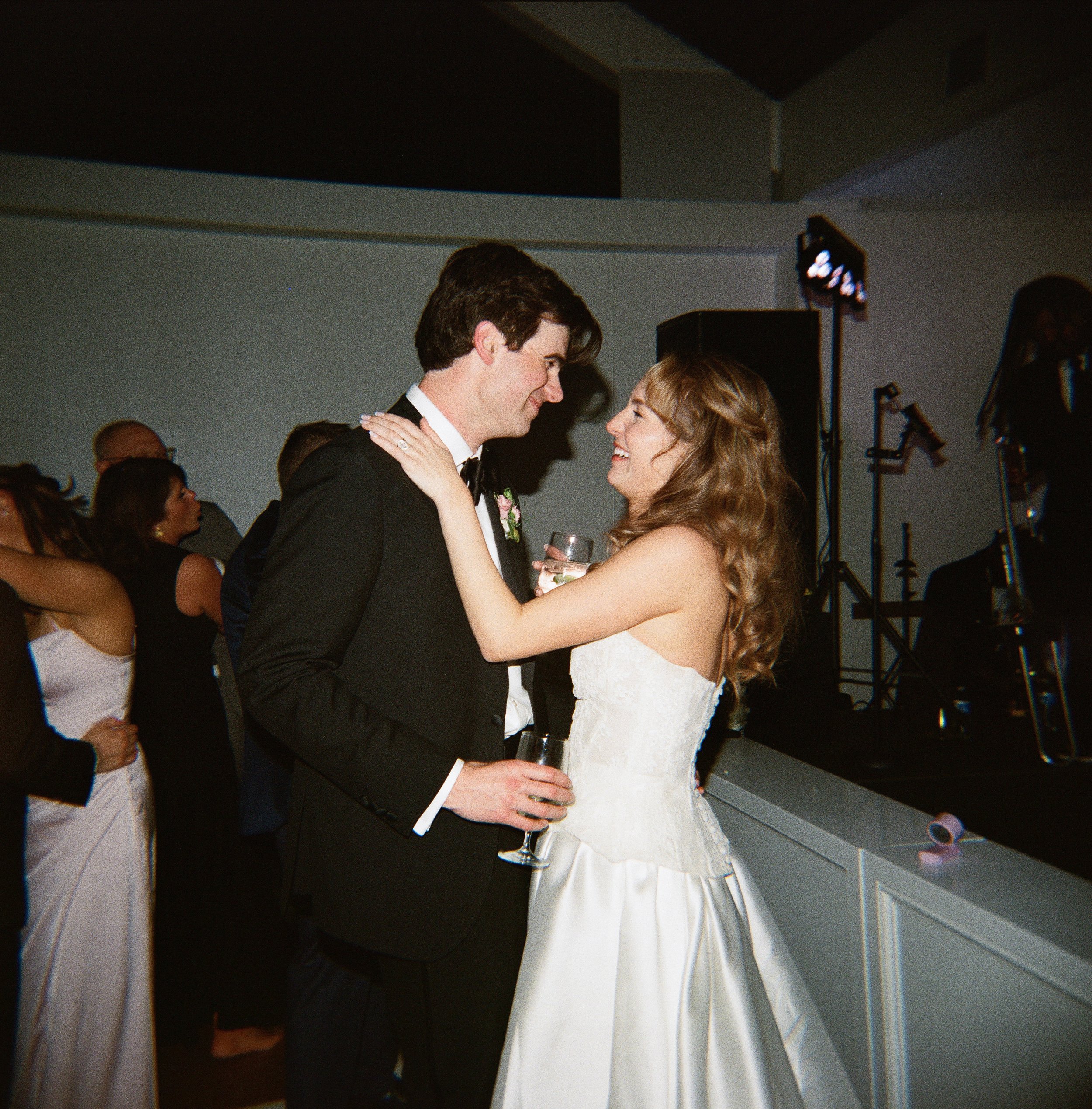 A couple dancing at a wedding reception, holding each other and smiling, with guests and event lighting in the background. richmond virginia wedding photographer