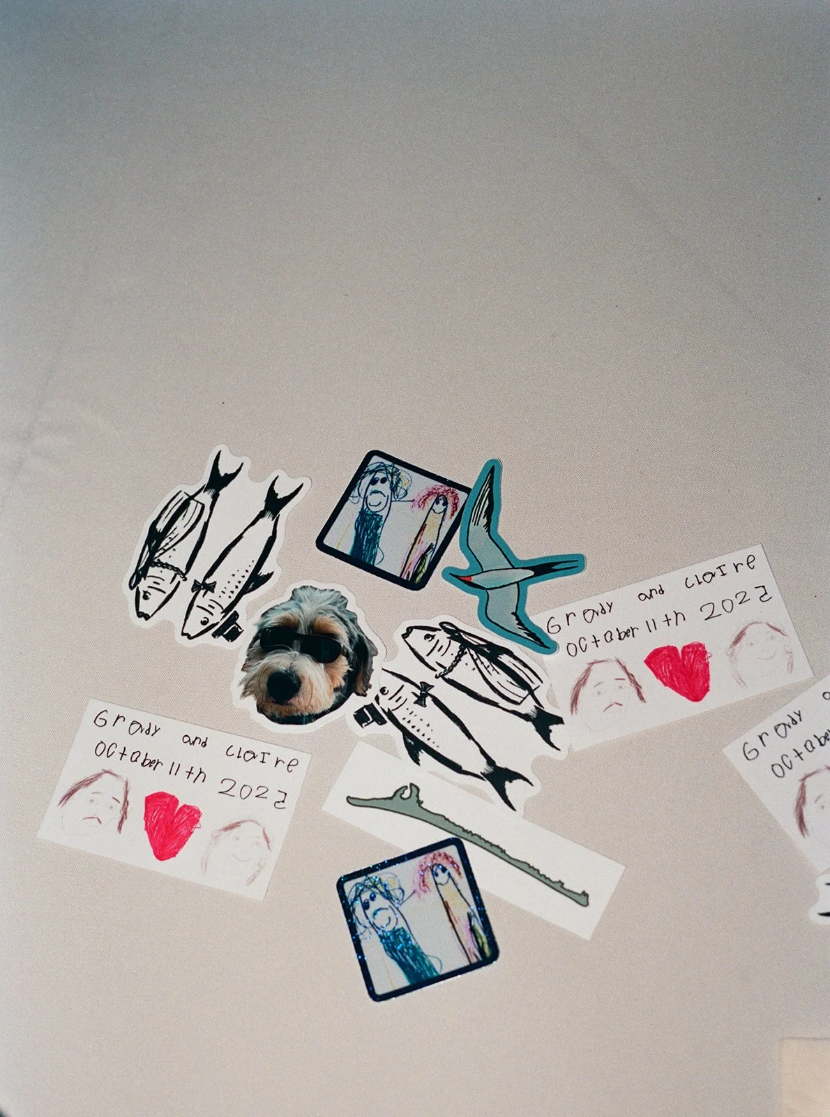 Decorative paper cutouts, drawings, and a dog wearing sunglasses arranged on a light-colored surface, with some handwritten notes and illustrations. ocracoke outerbanks wedding film photographer