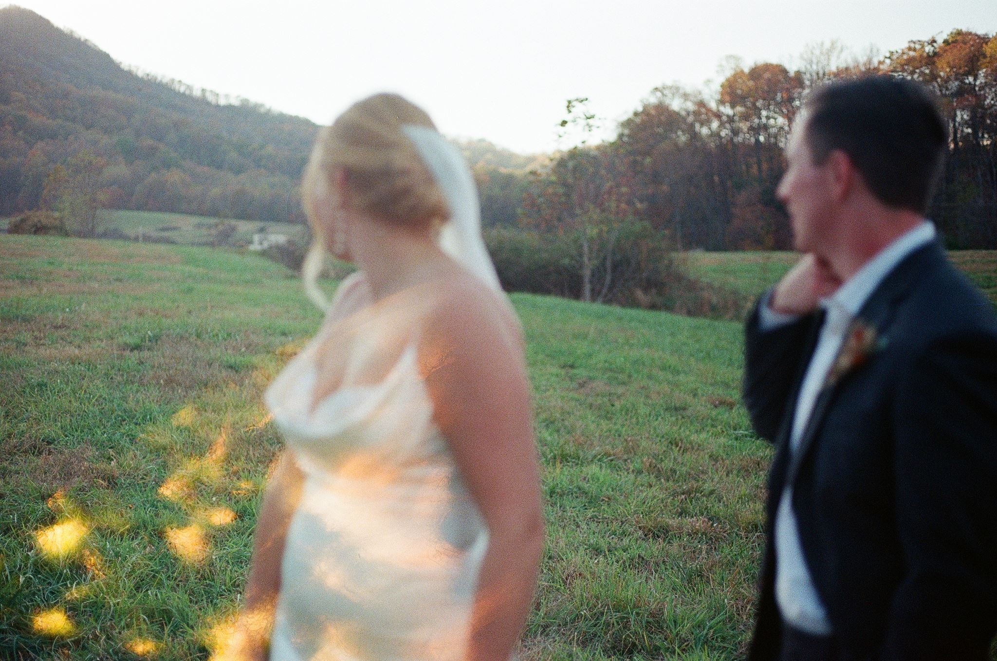 Blurred image of a woman in a wedding dress and a man in a dark suit facing each other outdoors, with trees and hills in the background. roanoke wedding film photographer virginia
