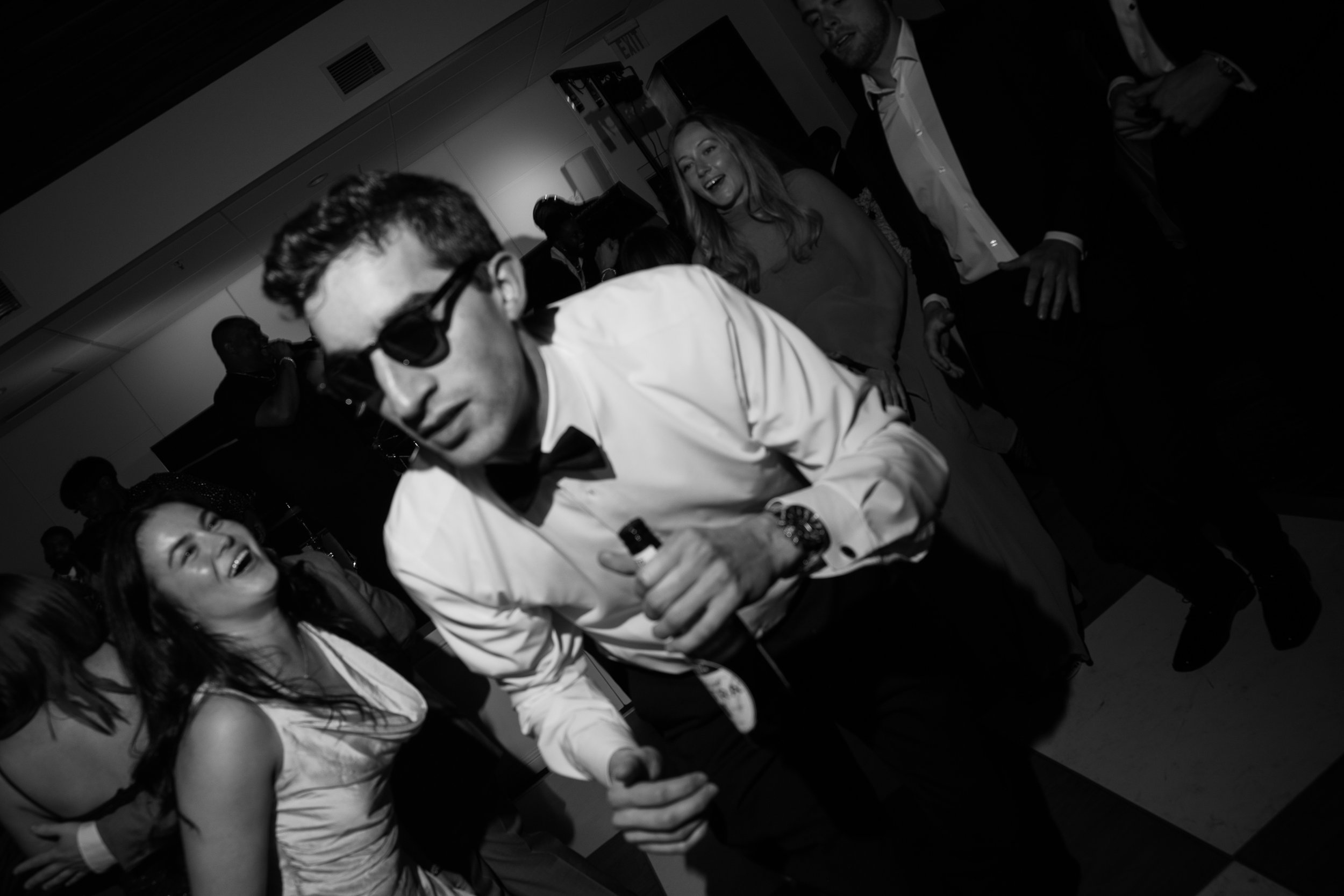 People dancing and socializing at a party in a dimly lit room, dressed in formal attire.