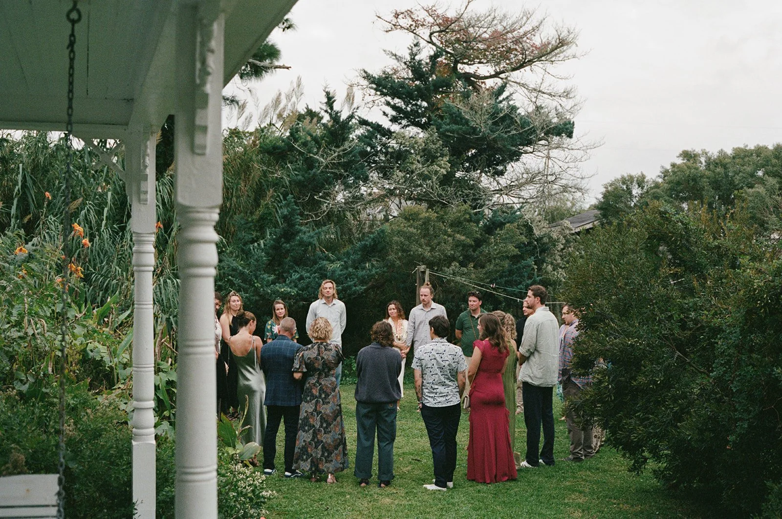 Group of people gathered outdoors in a garden, possibly for a ceremony or celebration, surrounded by trees and greenery. ocracoke outerbanks wedding film photographer