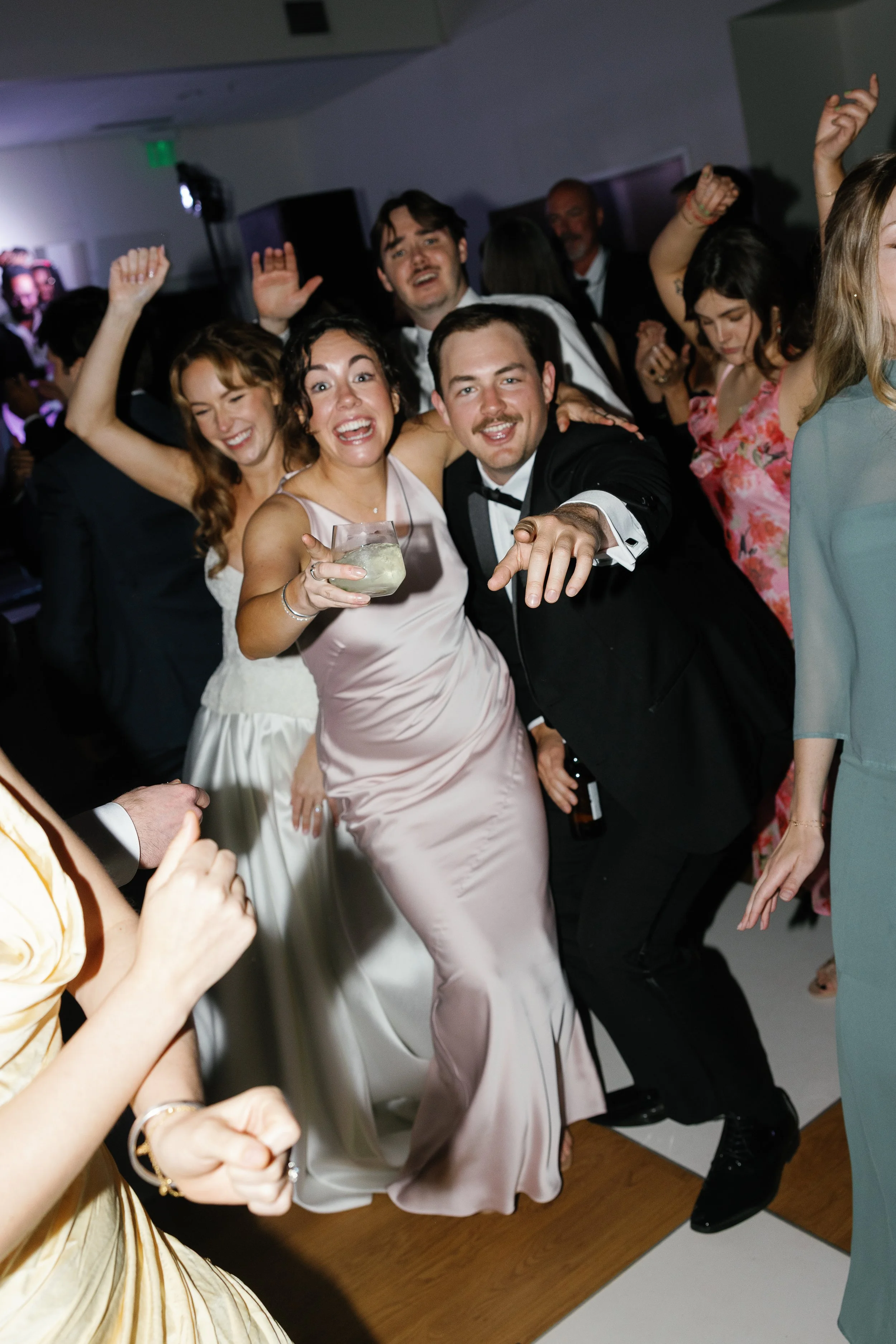 People dancing and celebrating at a party, with some holding drinks, smiling and enjoying the moment.