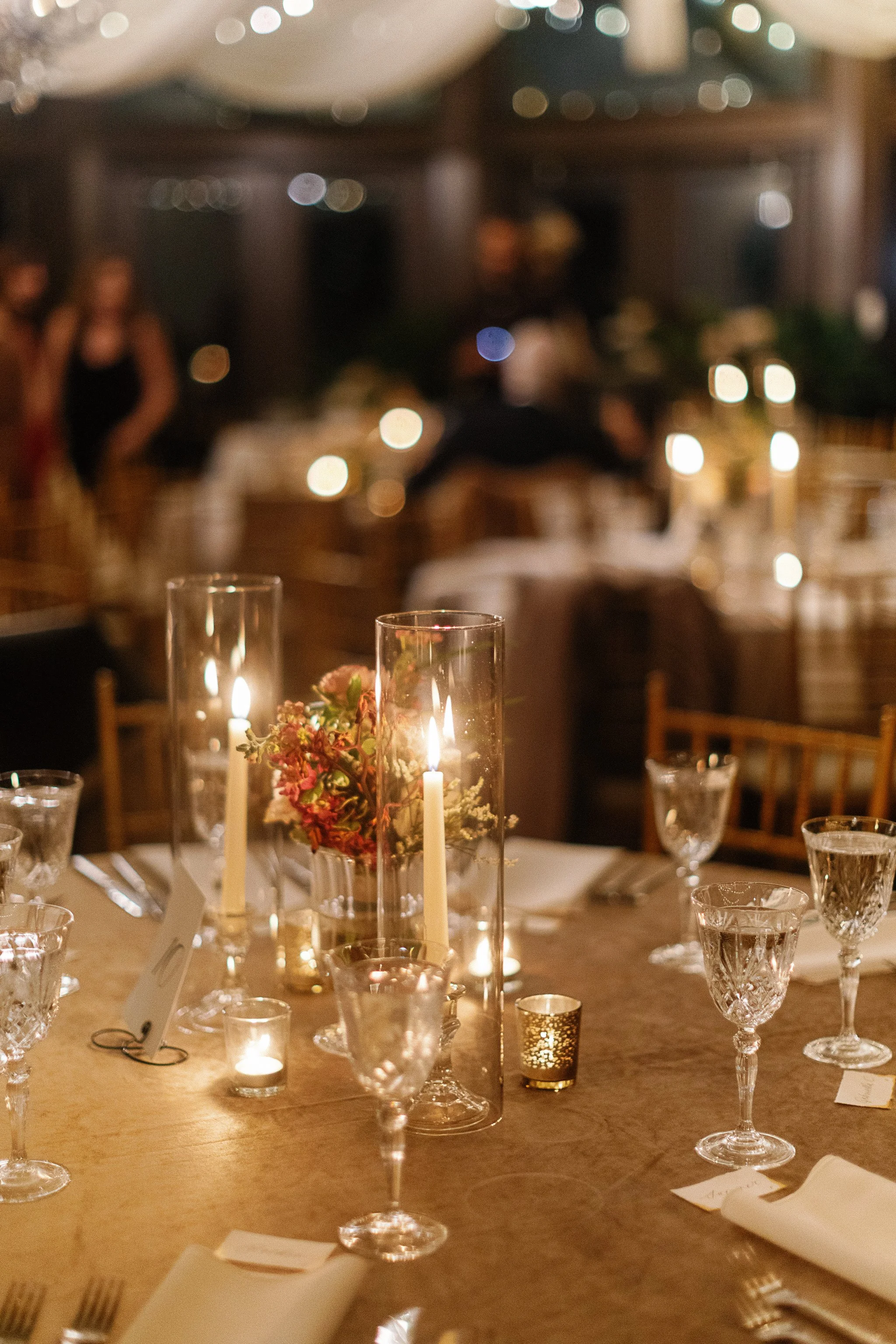 Elegant table setting with candles and crystal glassware at a dimly lit event, featuring floral centerpieces on a round table. gramercy mansion maryland wedding