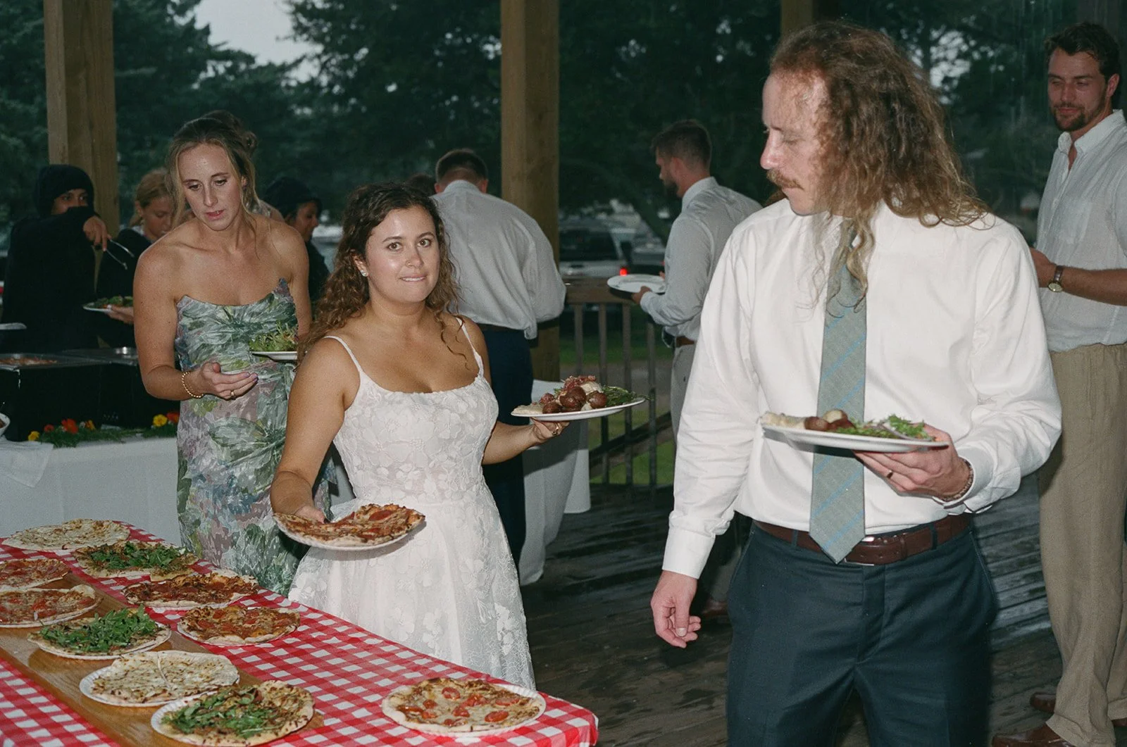 People at a buffet table eating pizza and salad at an outdoor gathering or party. ocracoke outerbanks wedding film photographer