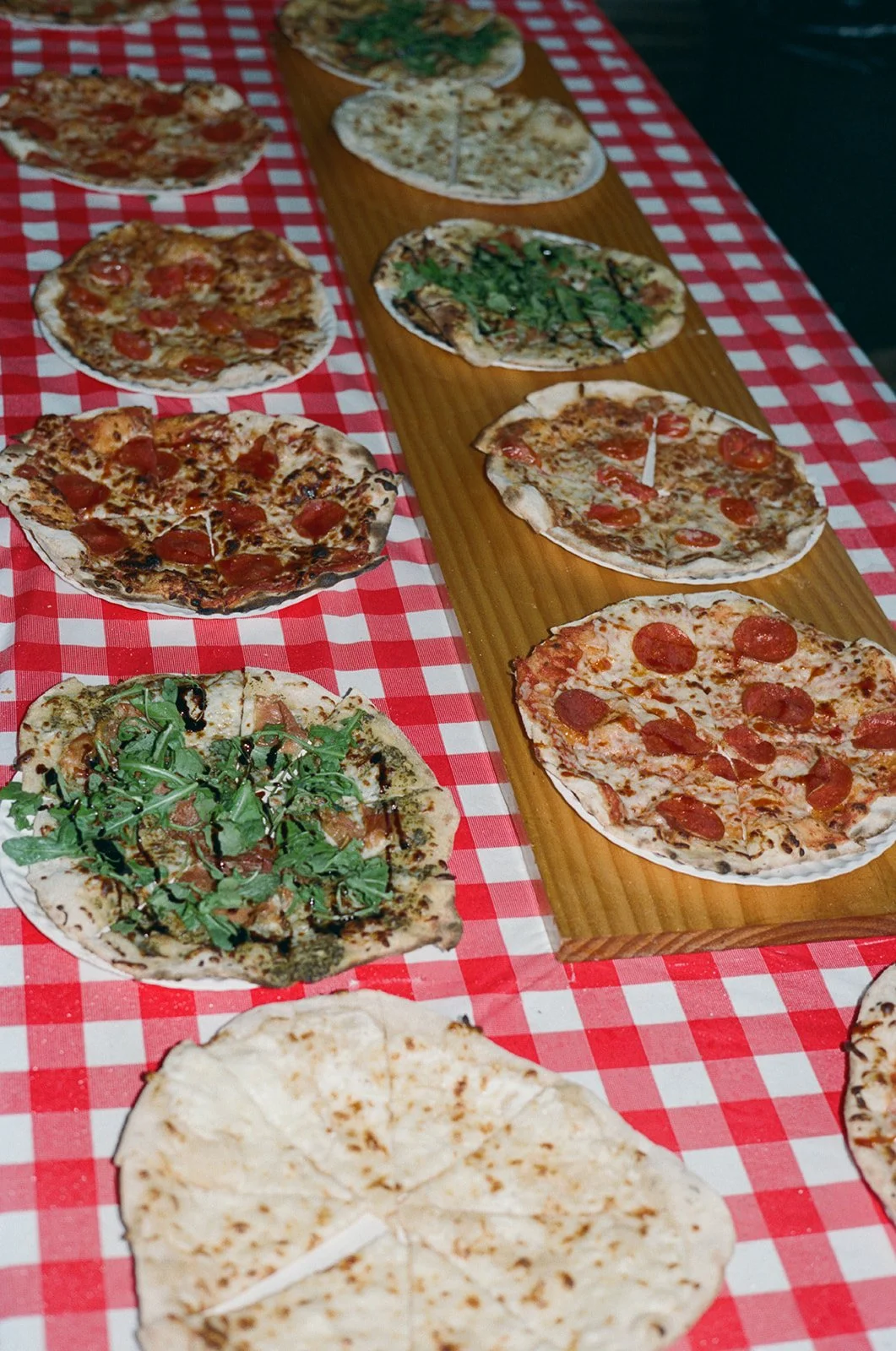 Various pizzas displayed on a checkered tablecloth and a wooden board. ocracoke outerbanks wedding film photographer