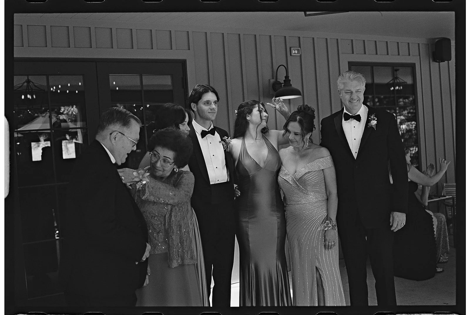 A black and white photo of people dressed in formal attire at a celebration or party, with a man in a tuxedo and a woman in a shiny gown at the center, surrounded by others in elegant dresses and suits. charlottesville virginia wedding photographer