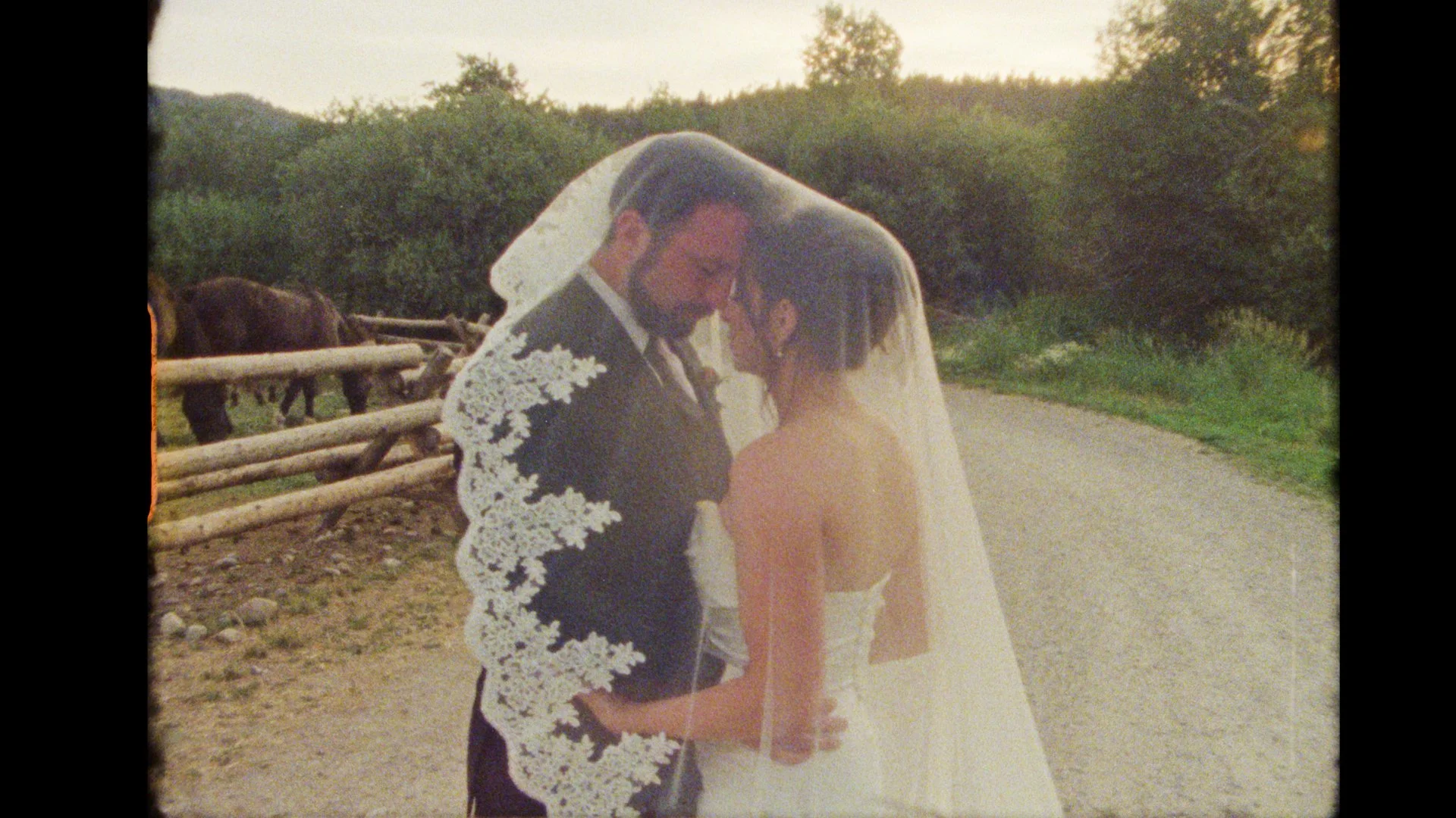 A bride and groom sharing a close, intimate moment outdoors, on their wedding day, with trees and a wooden fence in the background. moose creek ranch idaho