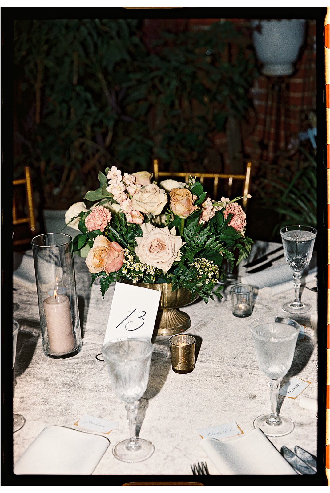 Elegant table setting with a central floral arrangement of roses and greenery, surrounded by wine glasses, candles, and place cards, at a formal event or dinner. Gramercy Mansion Maryland Wedding Film Photographer.