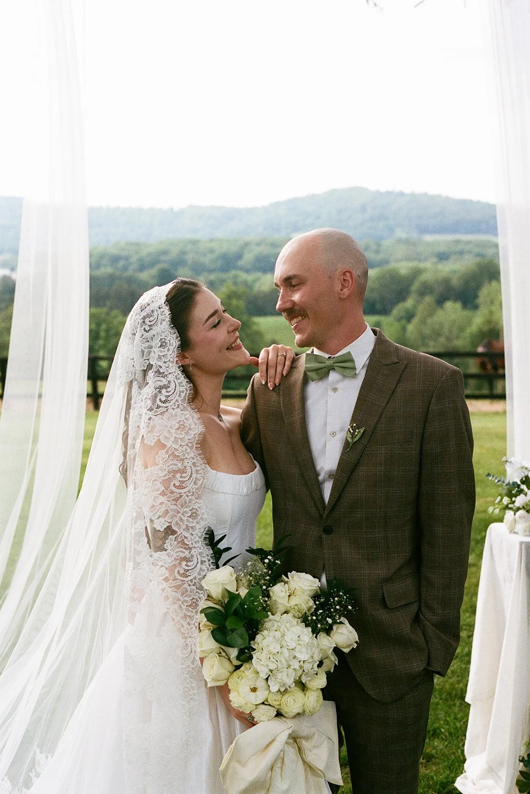 Bride and groom smiling at each other during outdoor wedding with scenic green landscape and Charlottesville Virginia hills in the background.