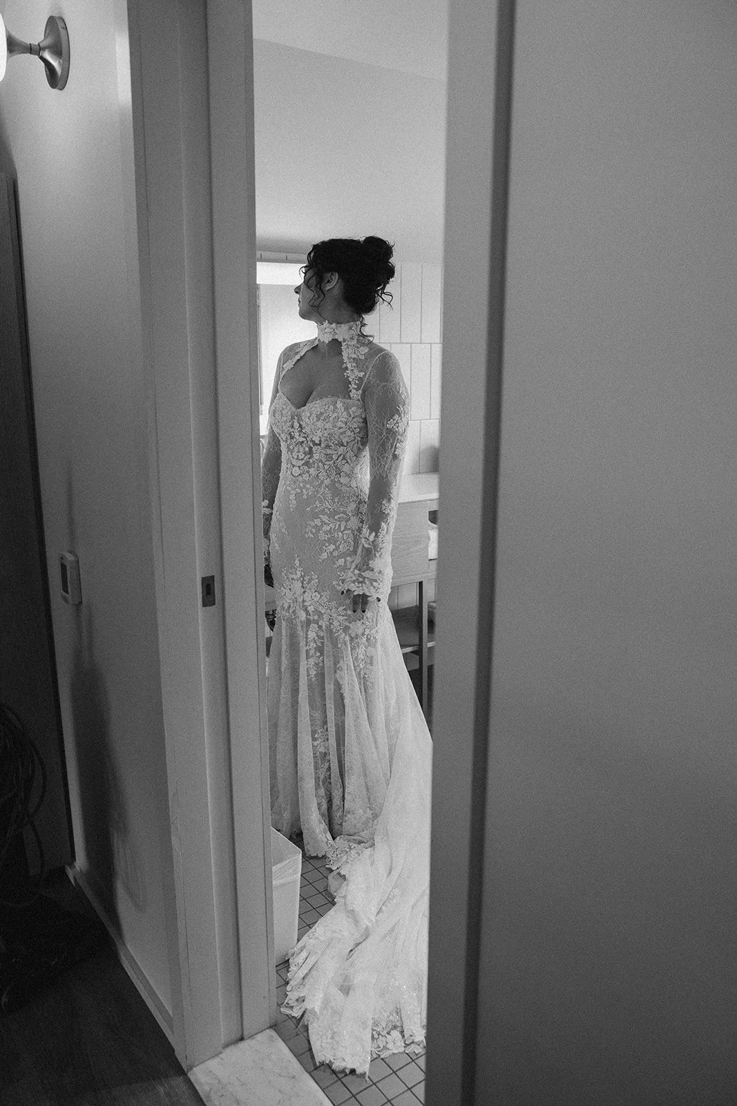 A woman in a lace wedding dress standing in a room, seen through a reflection in a mirror. doyle hotel charlottesville va