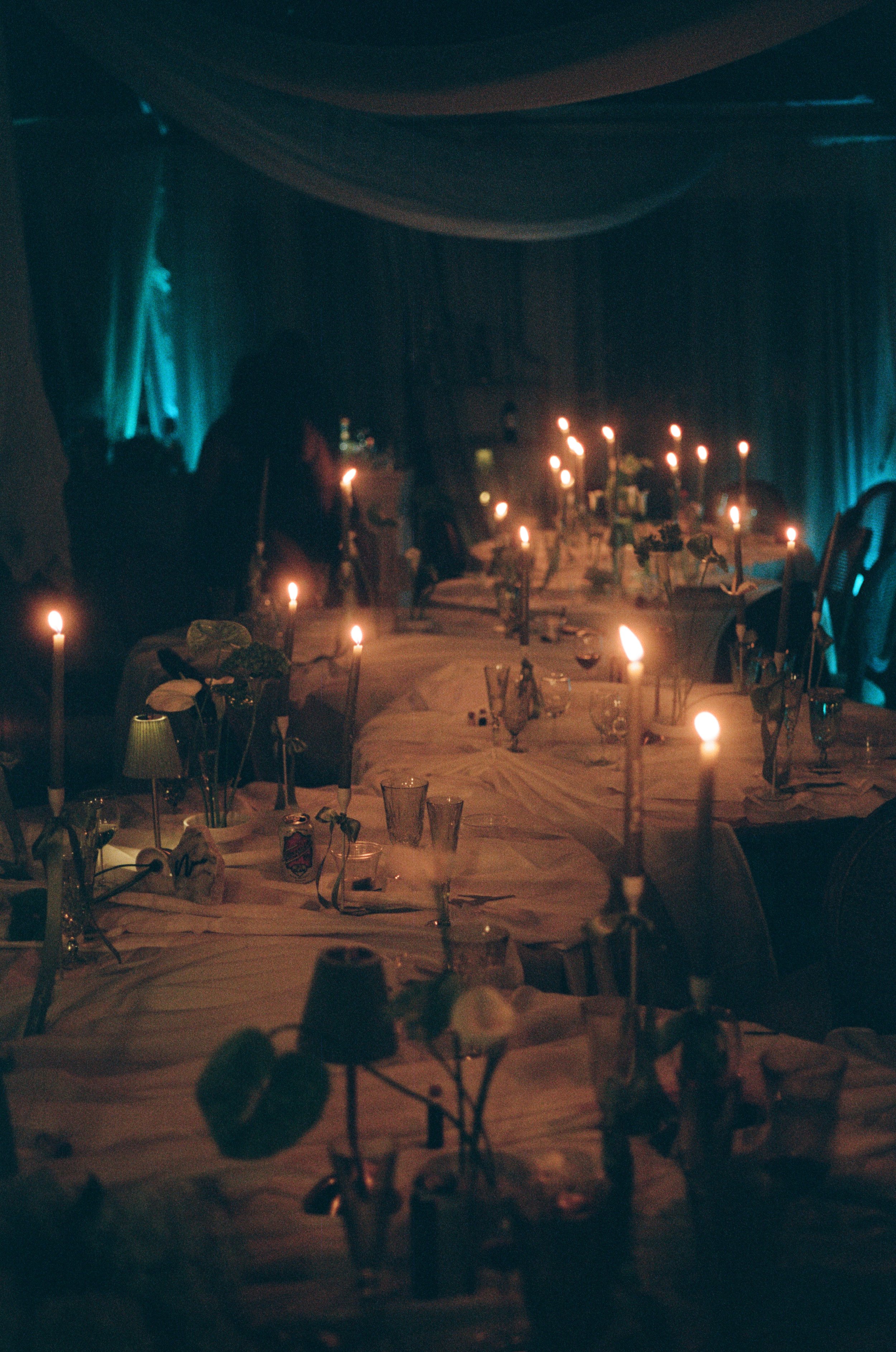 Dimly lit dining room with candles on a large table, set for a meal, with dark curtains and a blue-green glow in the background at High Torr Estate in Purcellville Virginia.