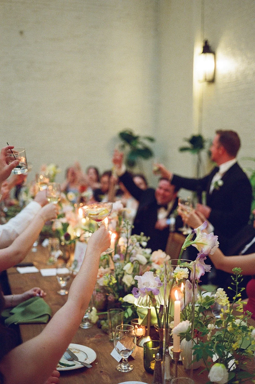 People raising glasses in toast at a wedding reception, with floral centerpieces and candles on a long table. The Engineers Club Baltimore Maryland wedding
