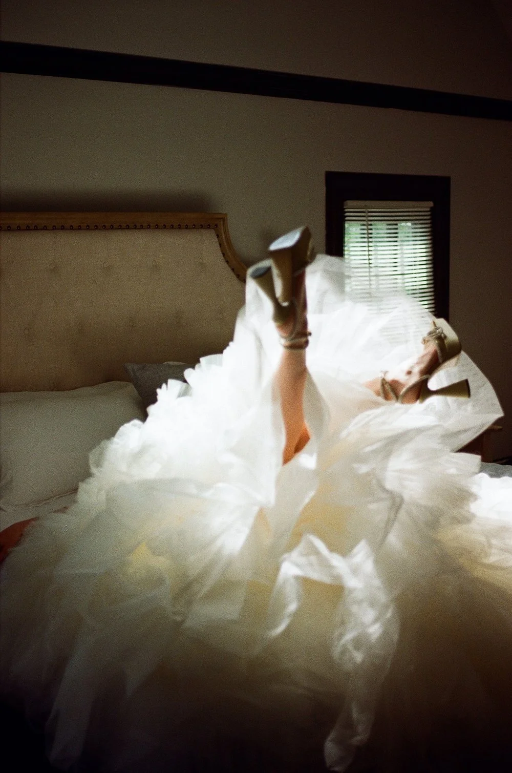Person in a fluffy white dress lying on a bed, with legs in the air wearing high heels.