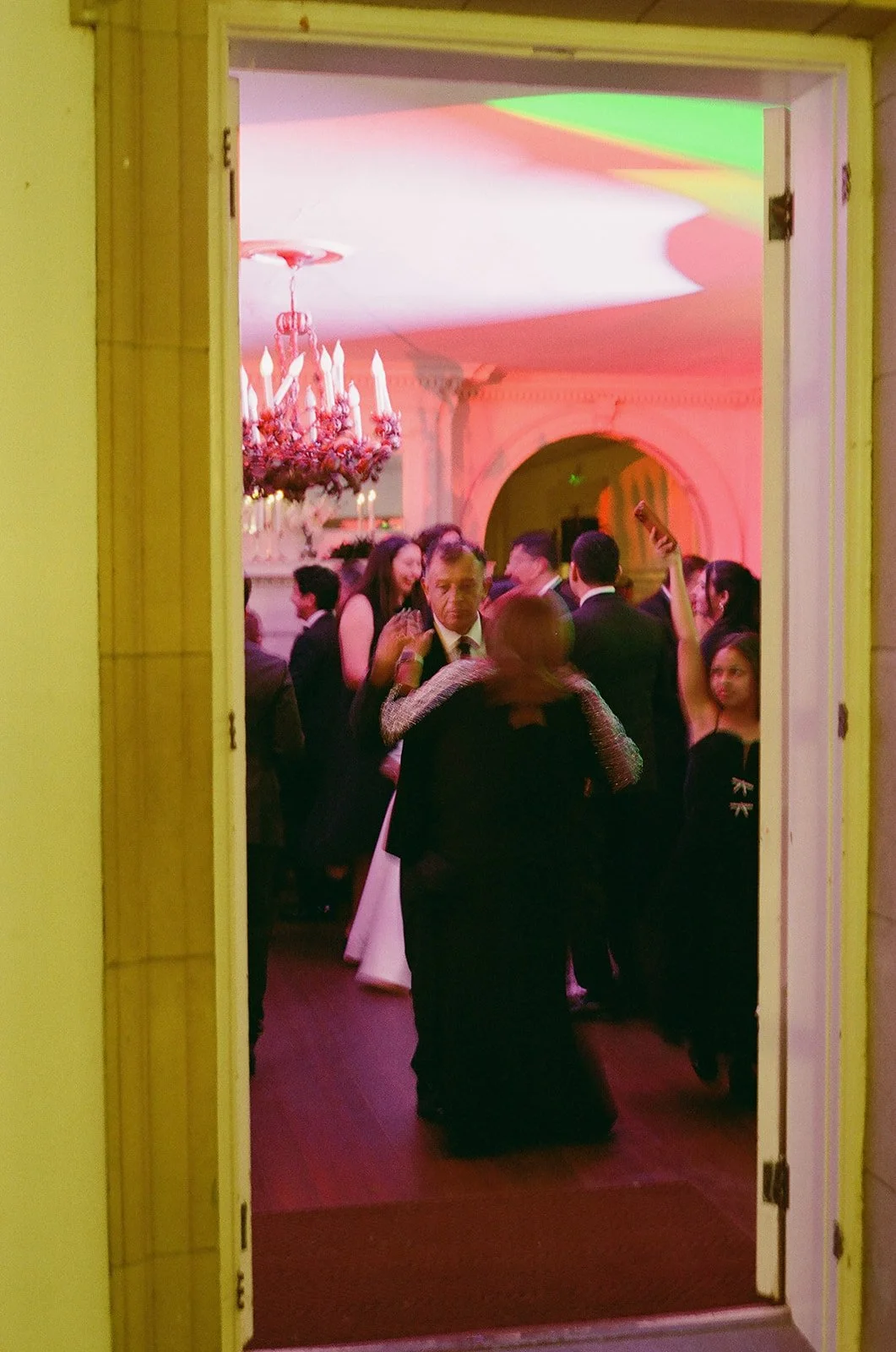People dancing and socializing at an elegant indoor party or event, seen through an open door.  Liriodendron Mansion Wedding Film Photographer