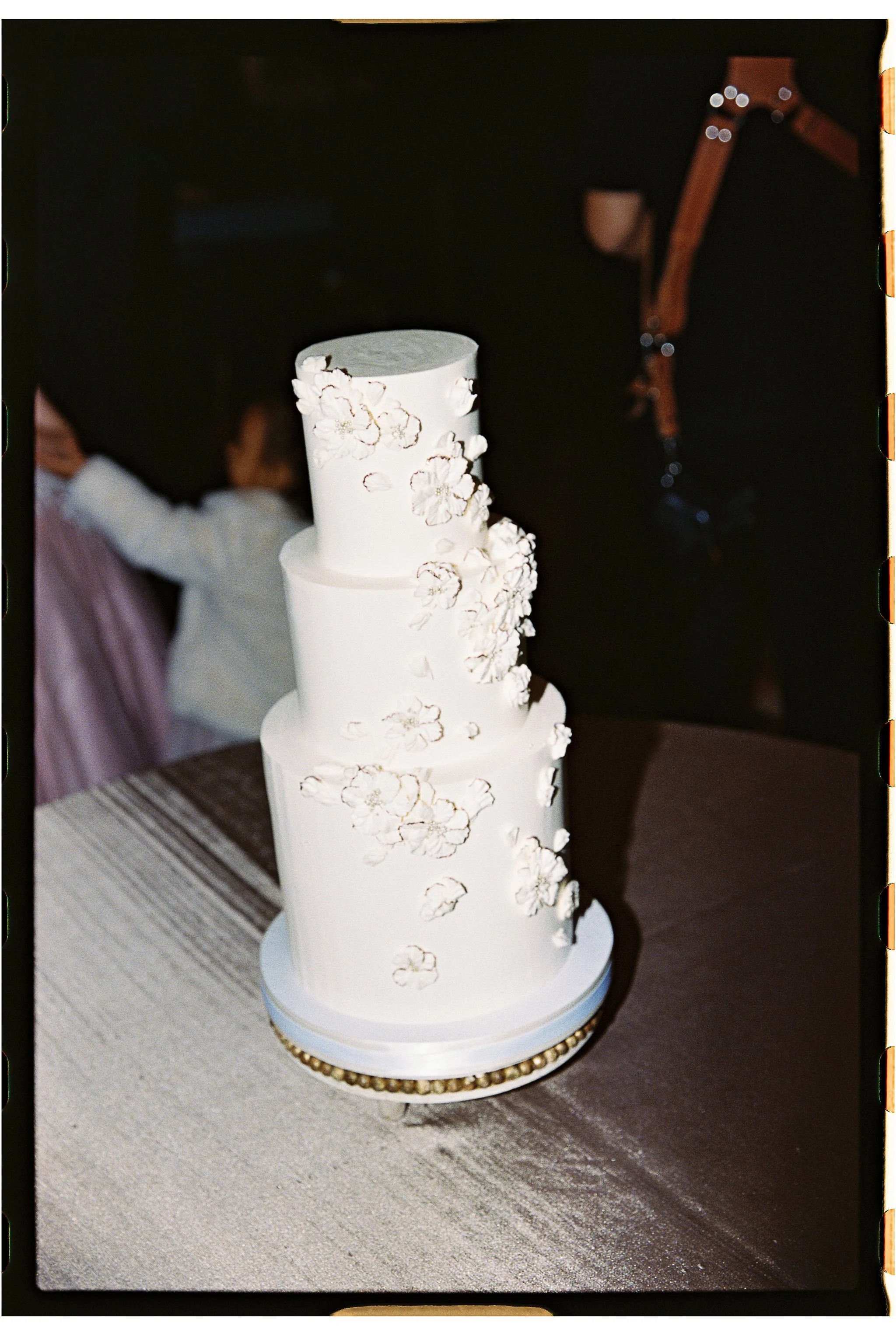 Three-tier white wedding cake with floral decorations on a table. gramercy mansion maryland wedding 35mm film