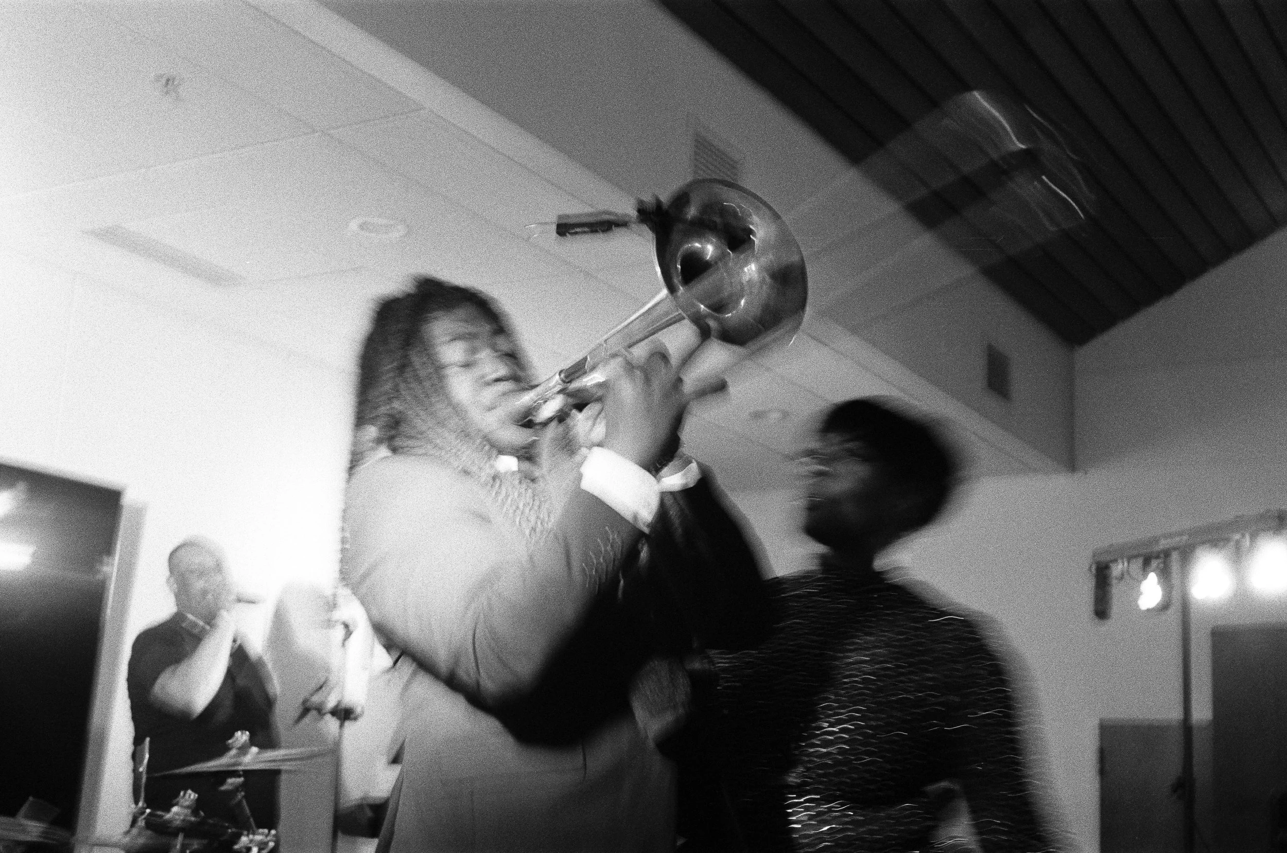 A woman playing the trombone at a social gathering with other people in the background.