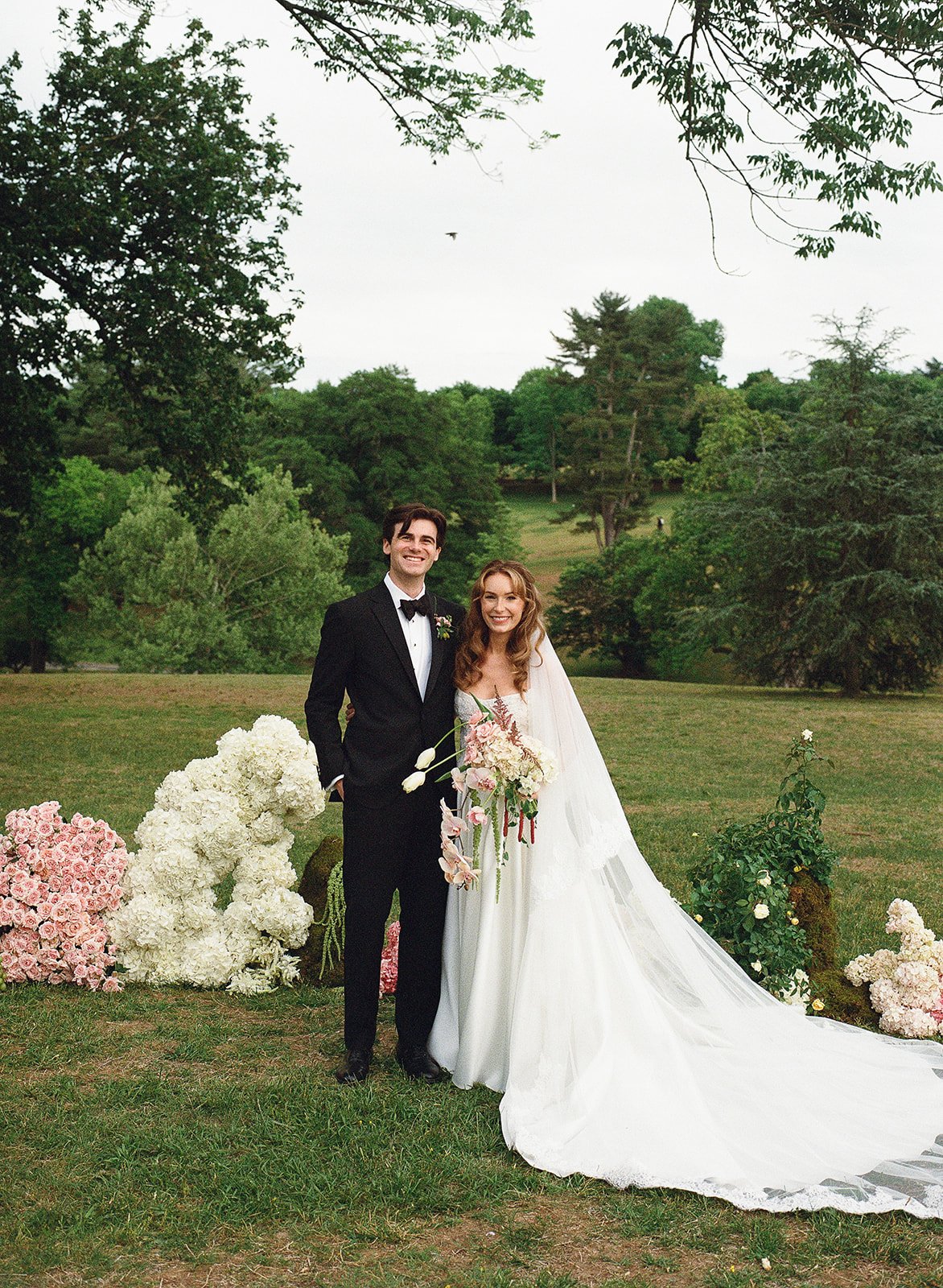 Maymont Richmond Virginia Wedding. Outdoor park pink white green florals. Bride and Groom standing in front of them smiling.