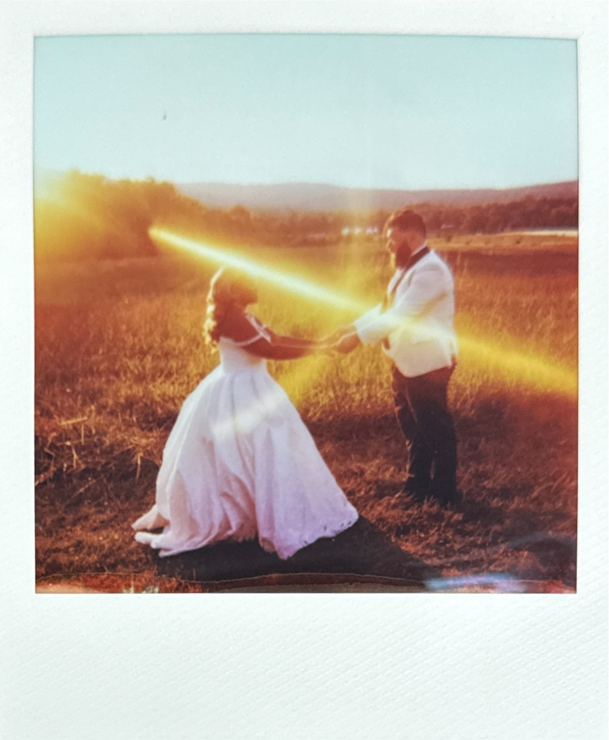A couple in formal attire holding hands in a field during sunset, with the woman kneeling and the man standing. Heigh Torr Estate Harpers Ferry Wedding Film Photographer