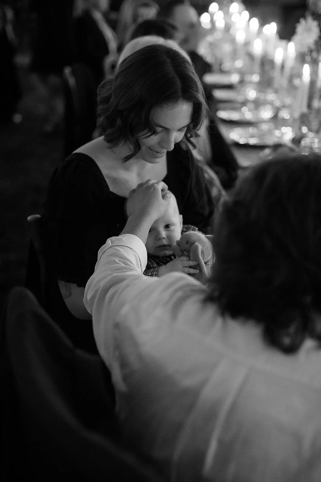 A woman holding a baby at a dinner table in a dimly lit restaurant. Roanoke Virginia Wedding Film Photographer.