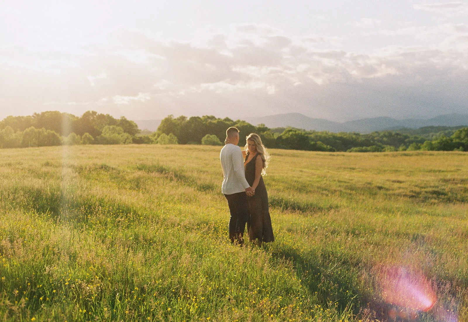 a couple holding hands at back creek valley overlook with the sun setting behind them