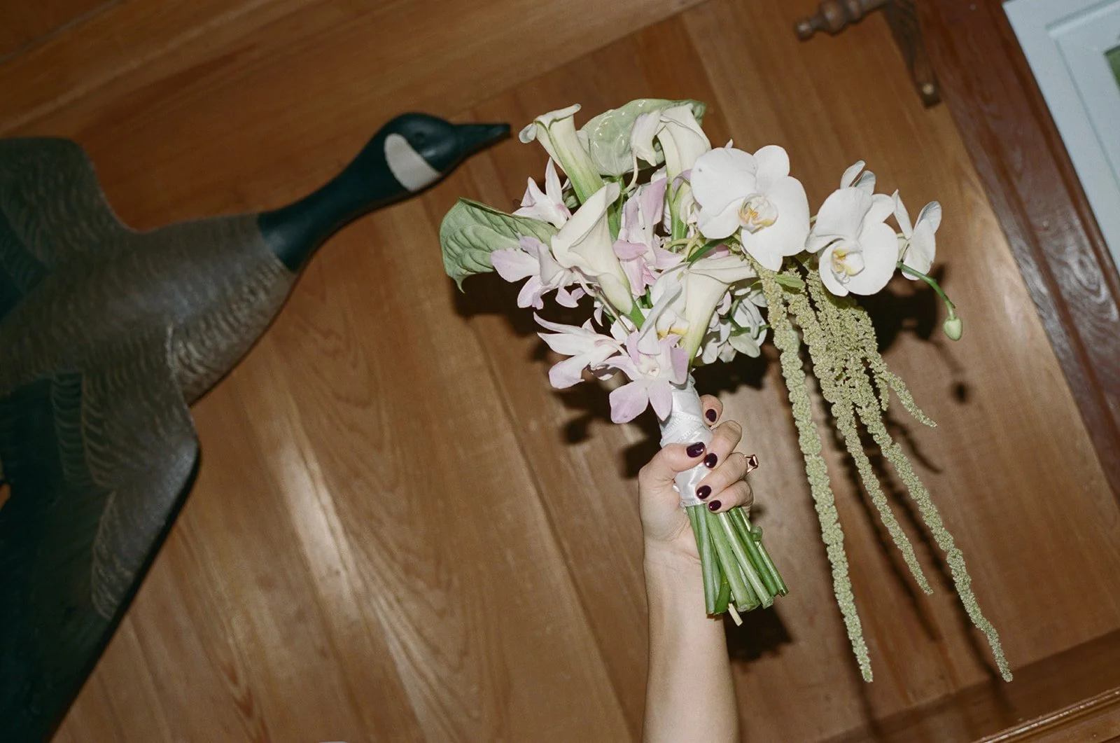 Hand holding a bouquet of pale pink and white flowers, including orchids and calla lilies, in front of a wooden wall. ocracoke wedding north carolina Wedding Film Photographer