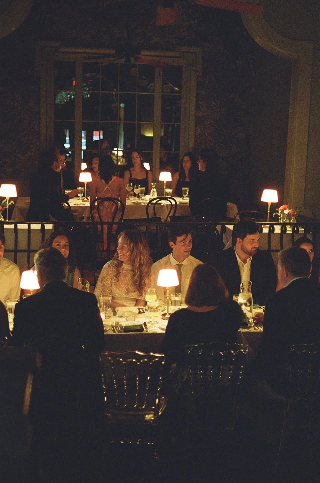 People dining at a restaurant with warm lighting and elegant decor, seated at a long table with candles and glasses. Chez Foushee Wedding Rehearsal Dinner Film Photographer Richmond Virginia