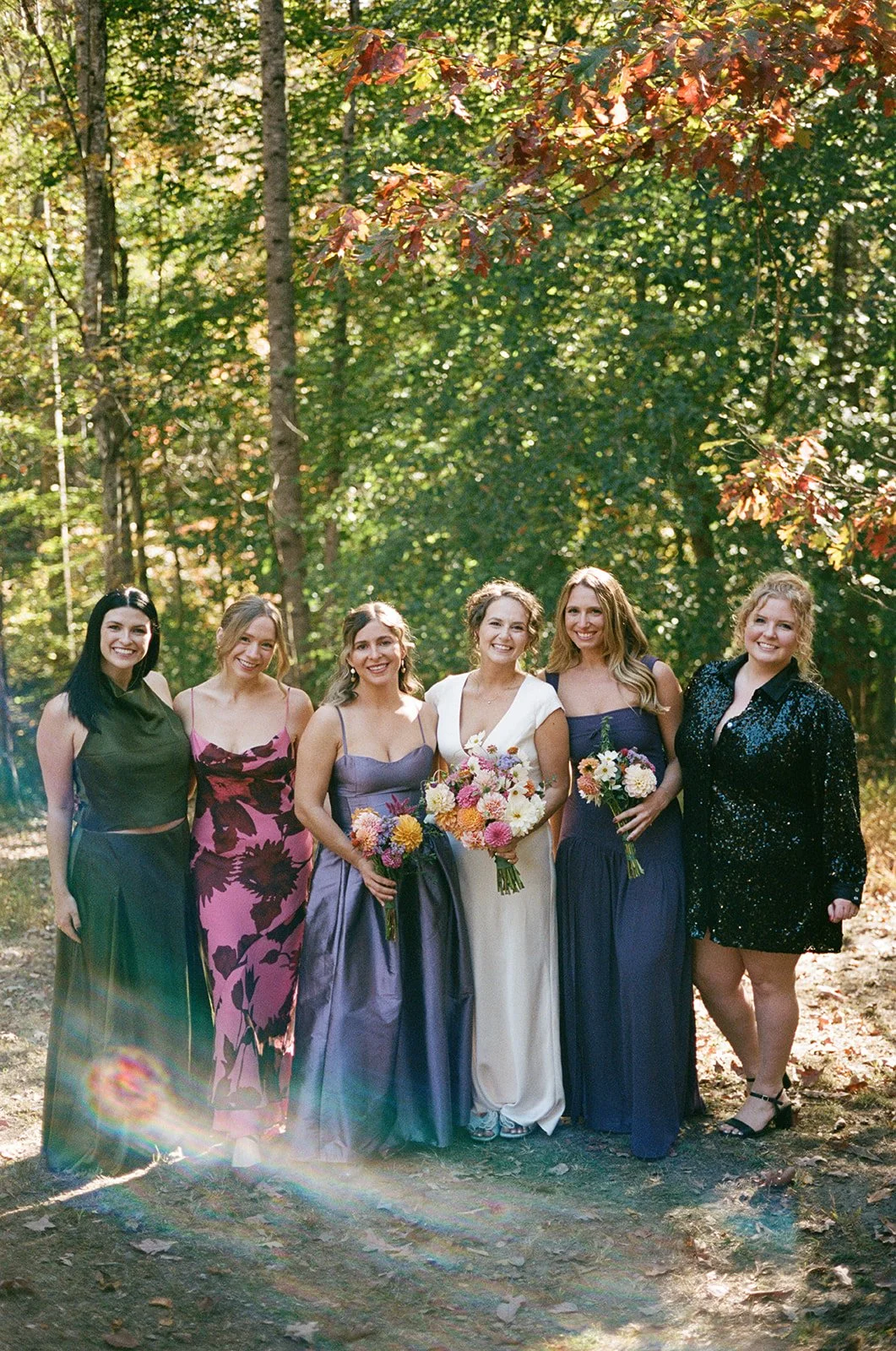 bride standing in the woods with 5 women dressed in wedding attire