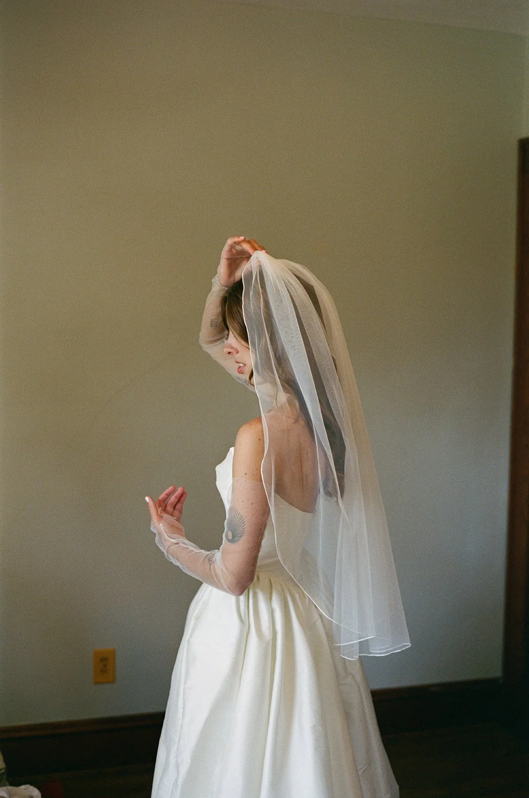 A bride in a white wedding dress and veil standing indoors against a plain wall. roanoke wedding film photographer virginia