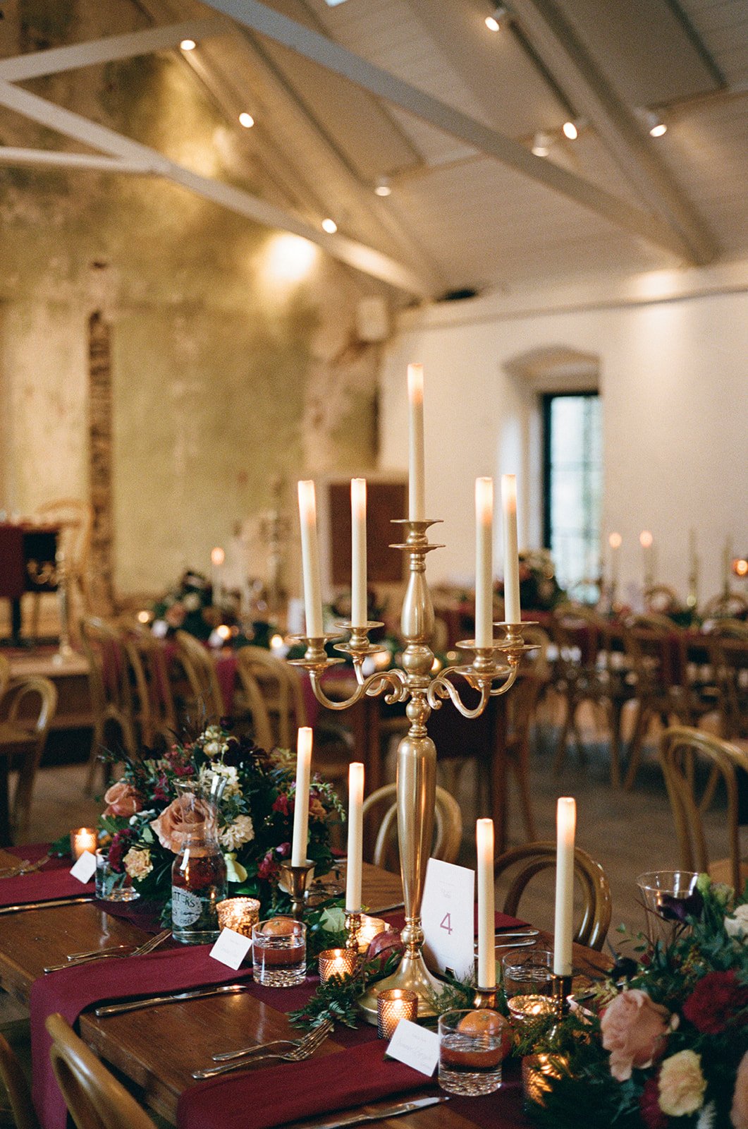 Decorated elegant wedding or event table with tall gold candelabrum, white candles, floral arrangements, and candlelit ambiance in a rustic venue. potters craft cider charlottesville va