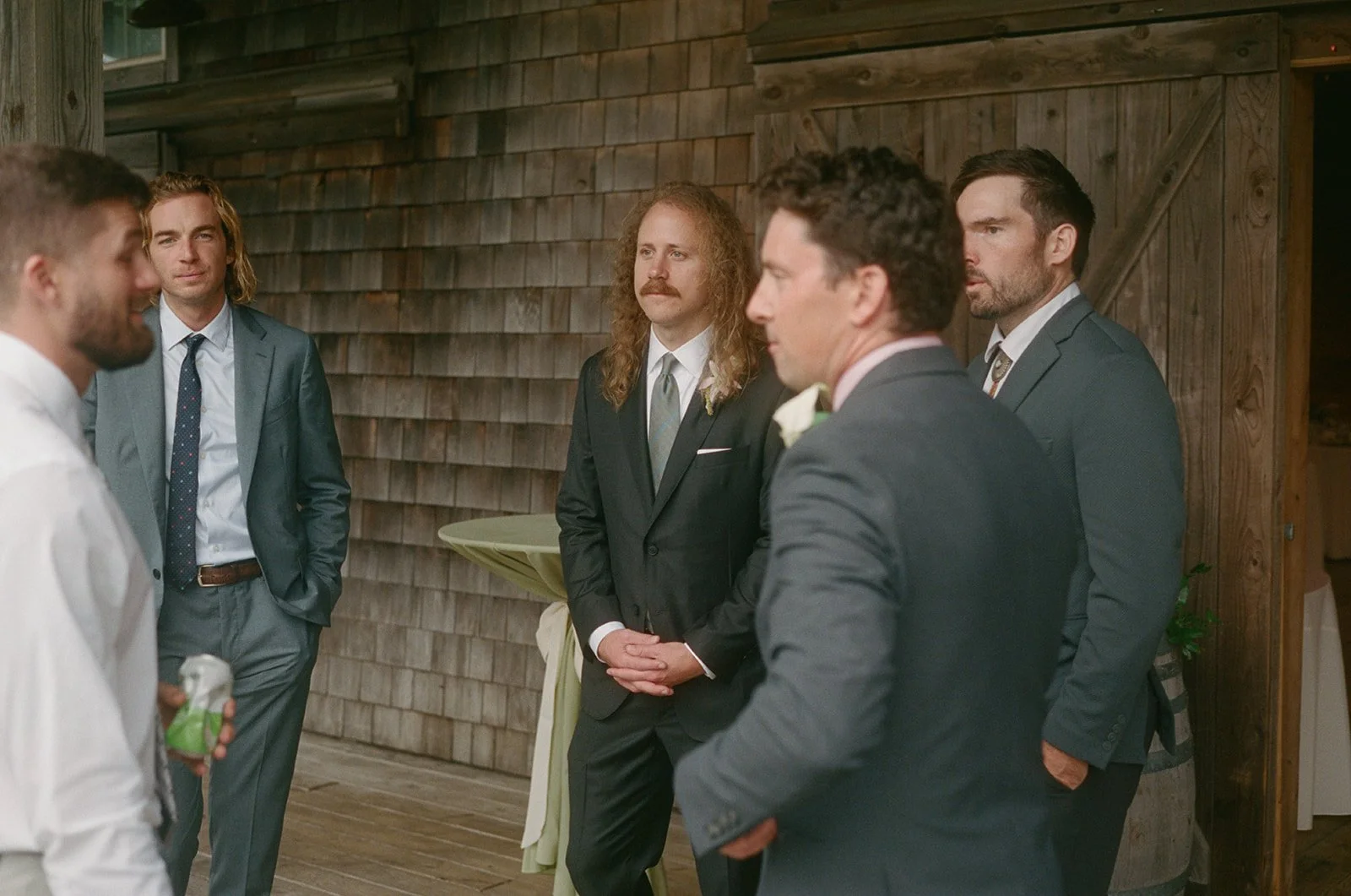 Group of men dressed in suits at a wedding or formal event indoors with wooden walls in the background. ocracoke outerbanks wedding film photographer