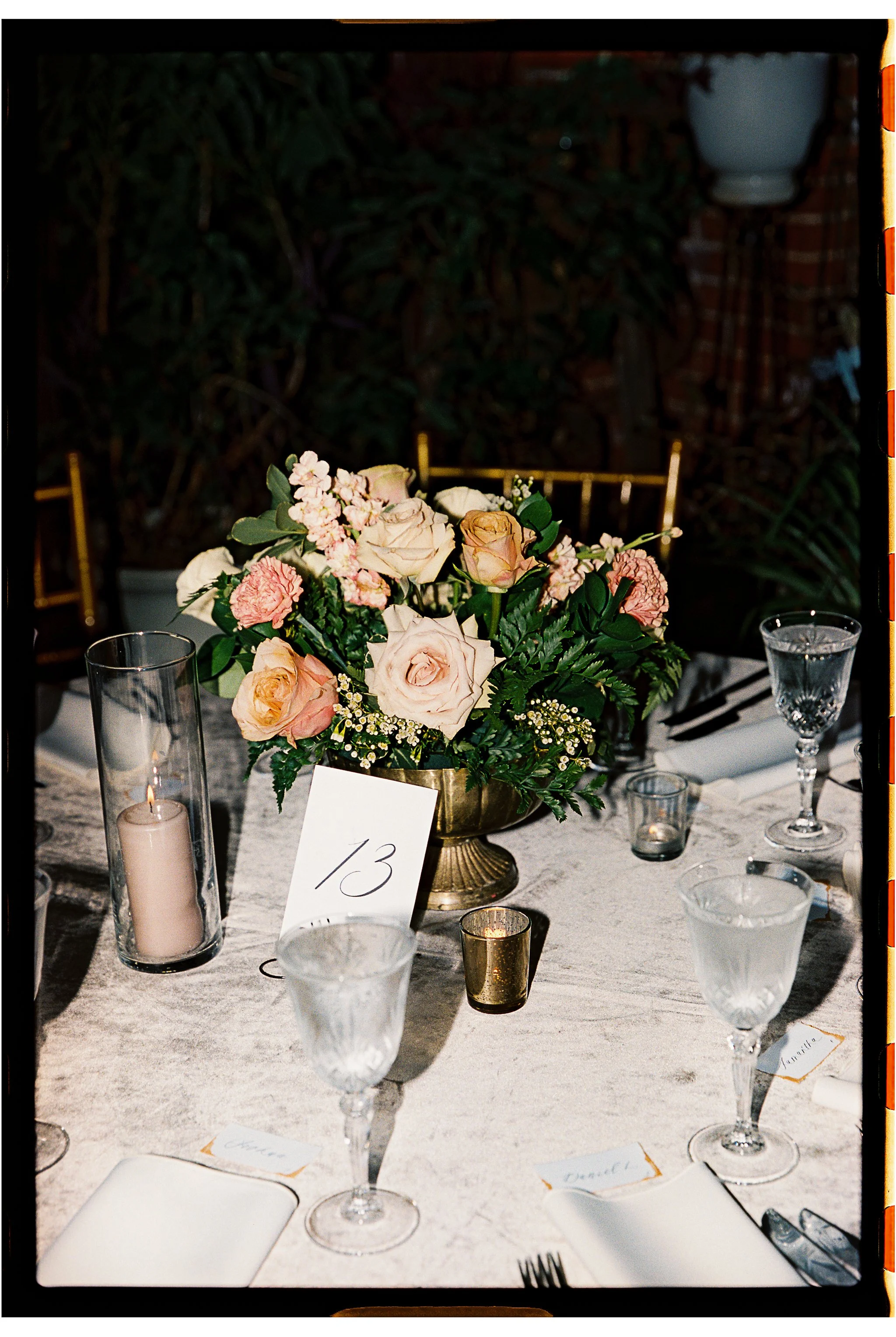 A dining table set for an event with a floral centerpiece, table number card 13, crystal glassware, and a lit candle in a glass holder. gramercy mansion maryland wedding