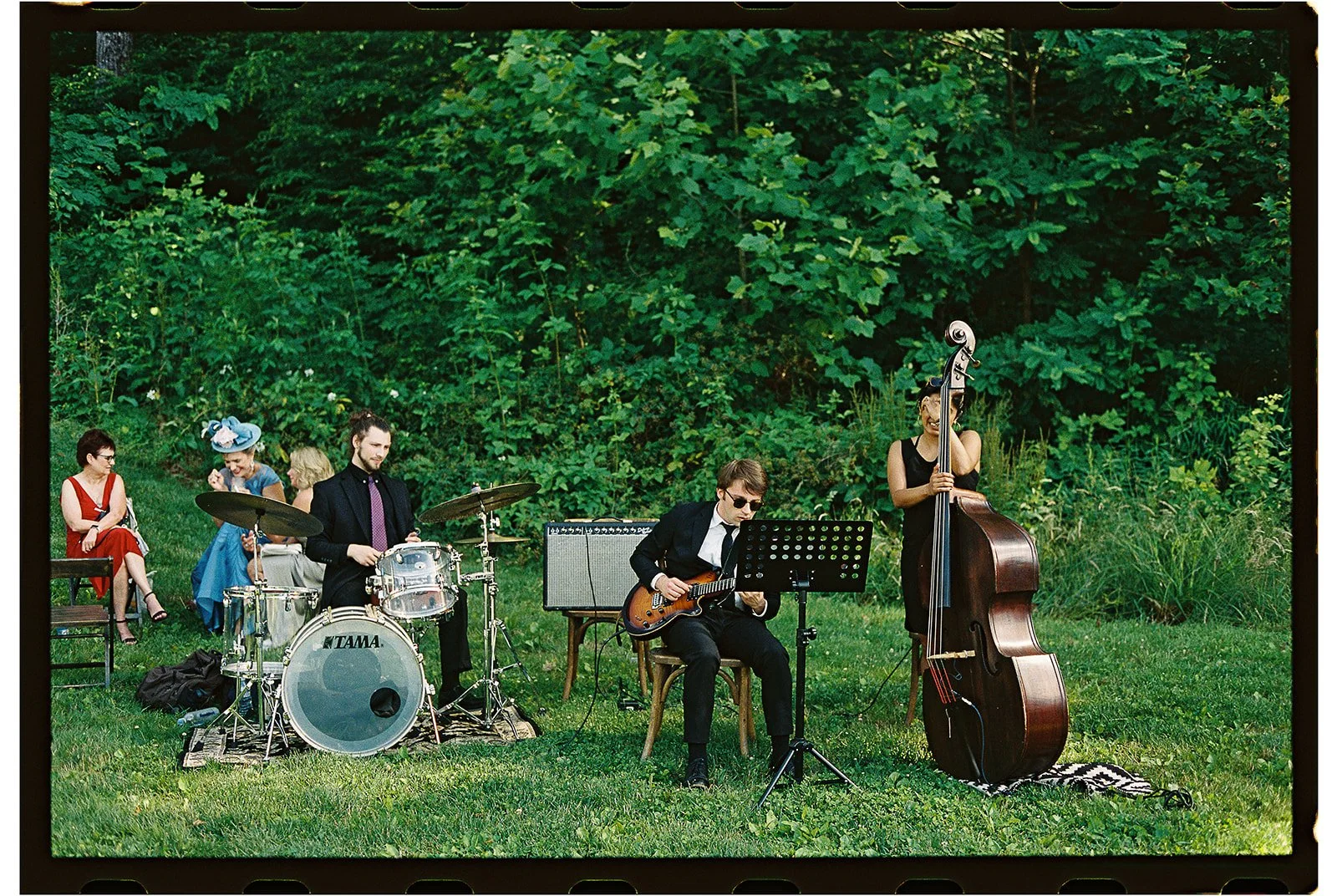 A group of four musicians playing jazz instruments outdoors on a grassy area with a lush green foliage background. charlottesville virginia wedding photographer eastwood winery
