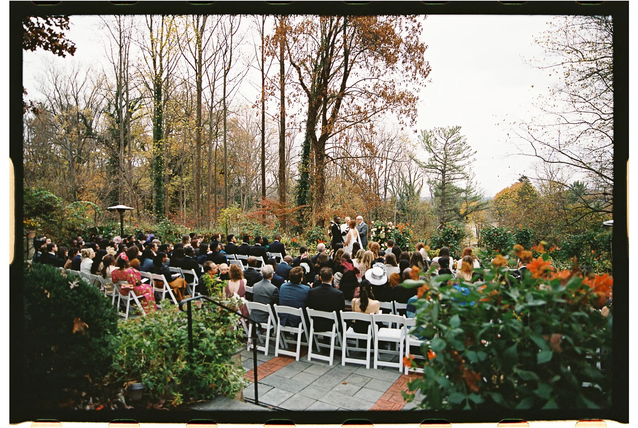Outdoor wedding ceremony with guests seated; couple and officiant at altar; autumnal trees in background. gramercy mansion maryland wedding
