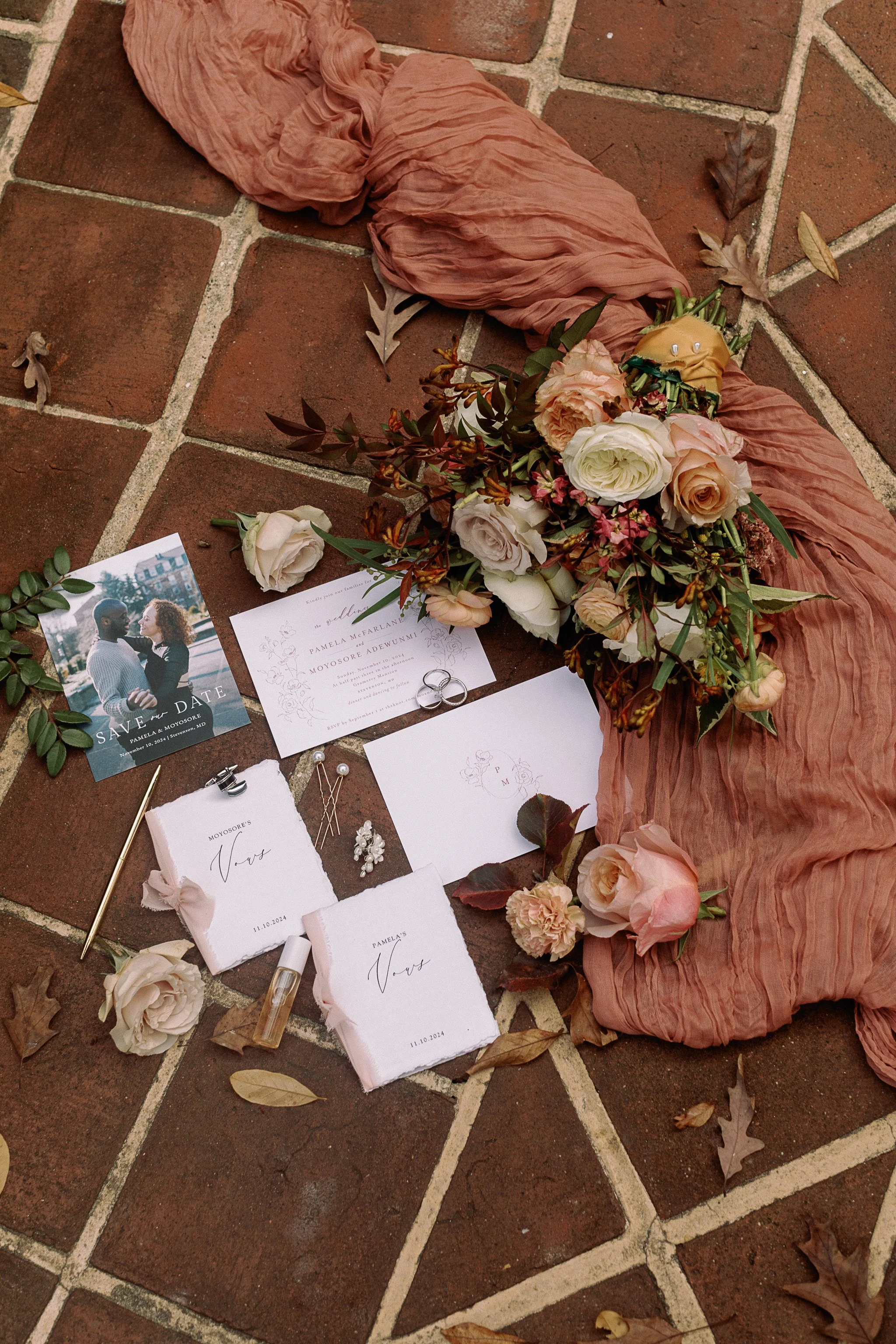 Wedding flat lay with bouquet, save the date card, wedding invitations, vow books, rings, and pink cloth on brick ground. gramercy mansion maryland wedding
