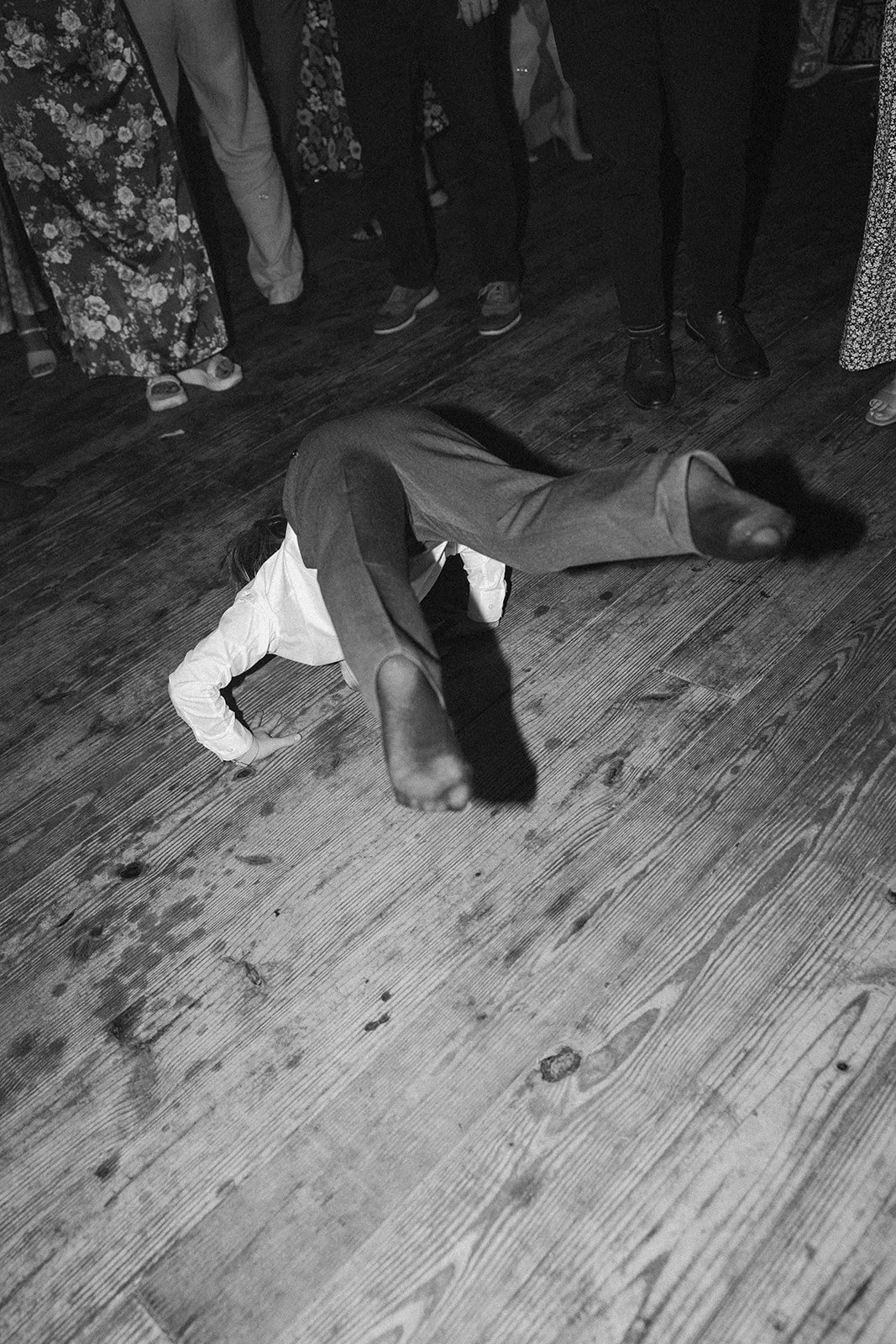A child performing a handstand on a wooden floor surrounded by people at a social gathering. ocracoke outerbanks wedding film photographer