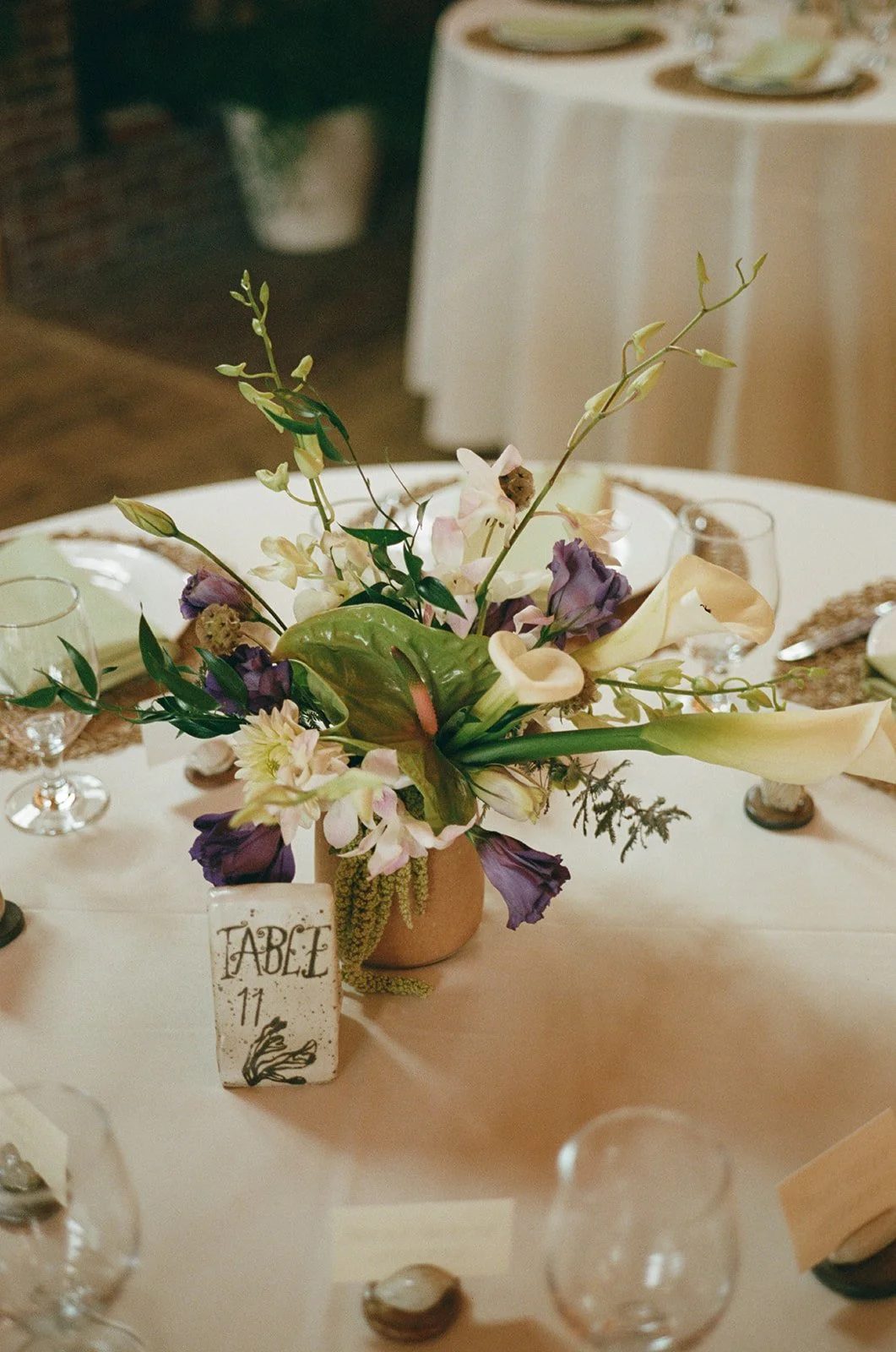 Flower centerpiece with purple, white, and green flowers on a dining table, labeled with a table number sign reading 'TABLE 11'. ocracoke outerbanks wedding film photographer