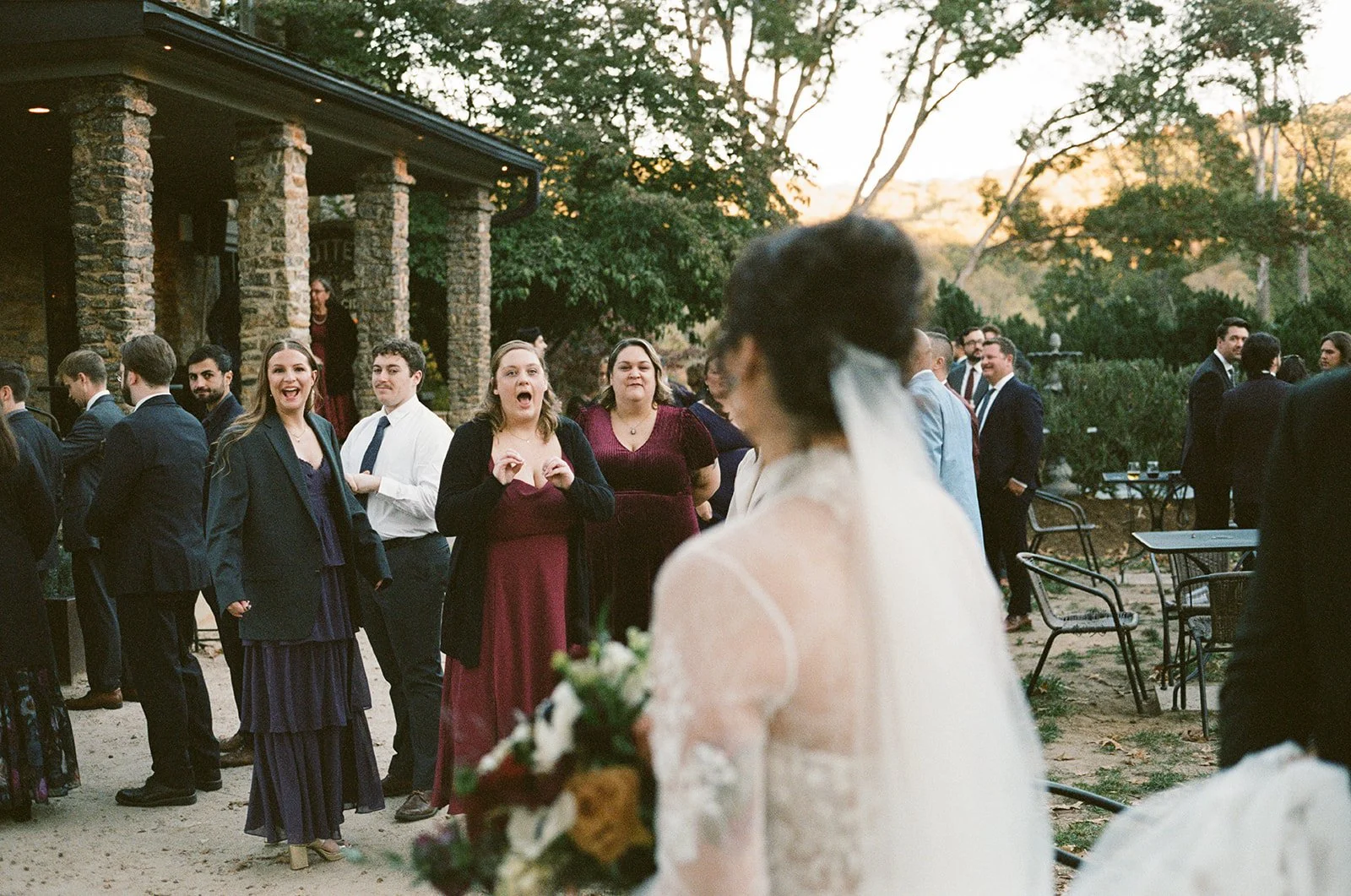 A bride with a bouquet looking at wedding guests socializing outdoors in the evening setting potters craft cider charlottesville va