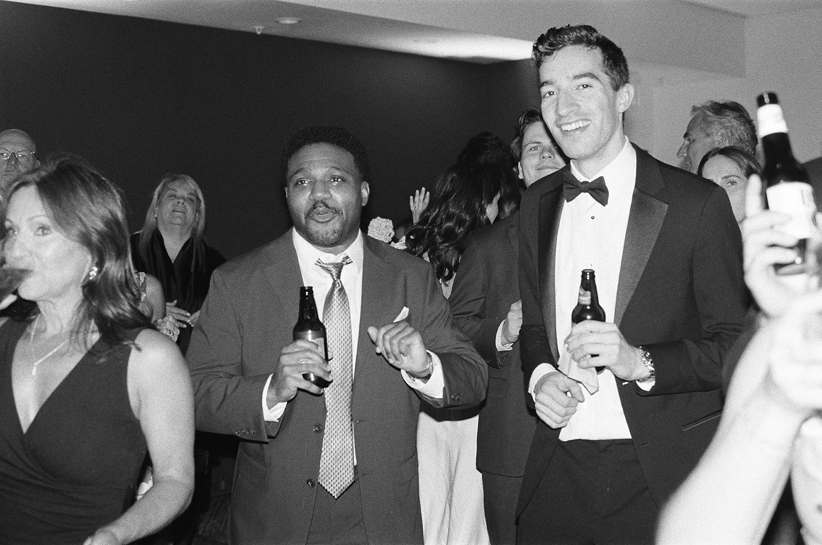 Several people in formal attire at a celebration, drinking beer, in an indoor setting with a dark background.  richmond wedding film photographer virginia
