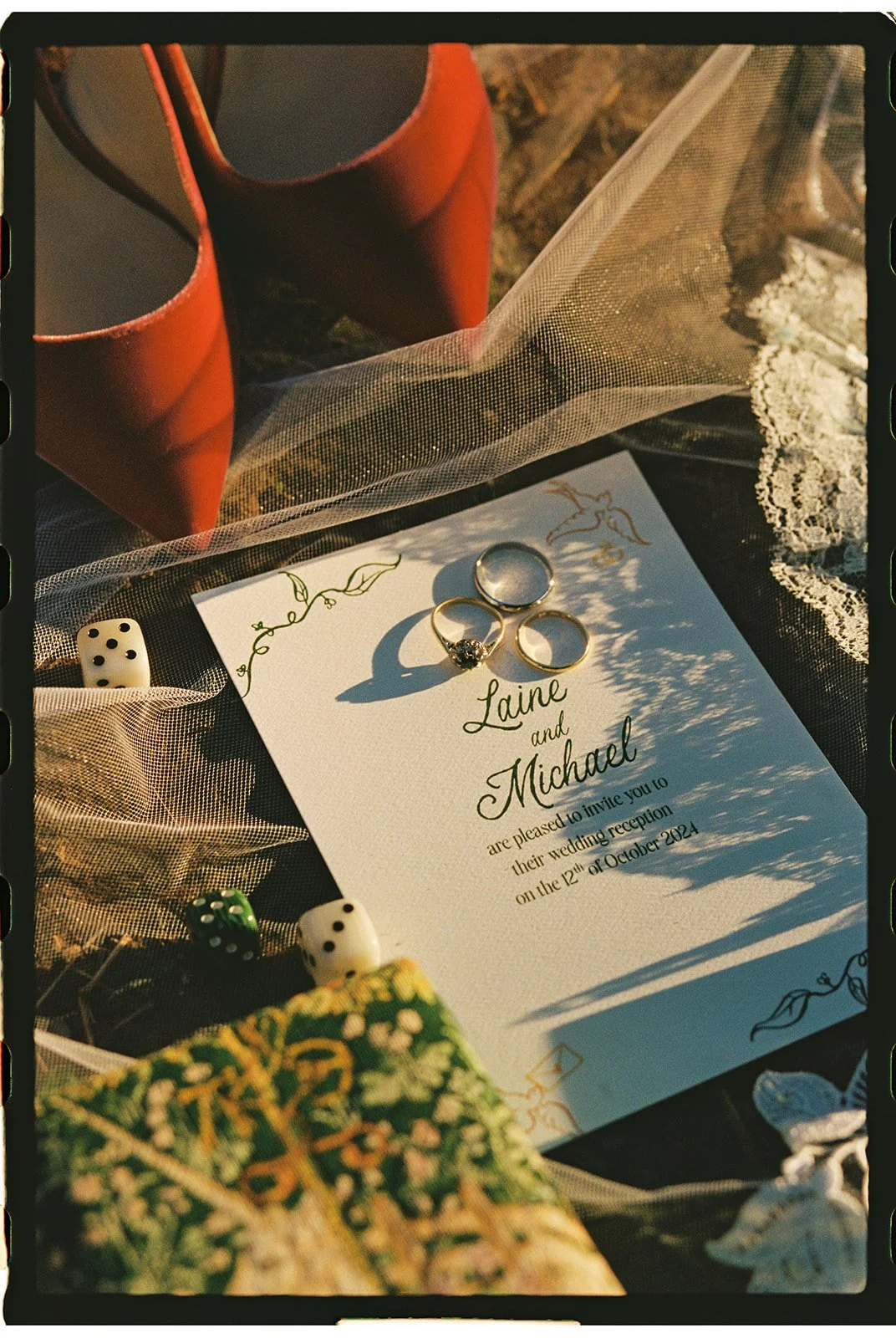 Wedding invitation for Laine and Michael, surrounded by three rings, two dice, a bouquet, and red shoes, with lace and tulle fabric. Roanoke Virginia Wedding Photographer.
